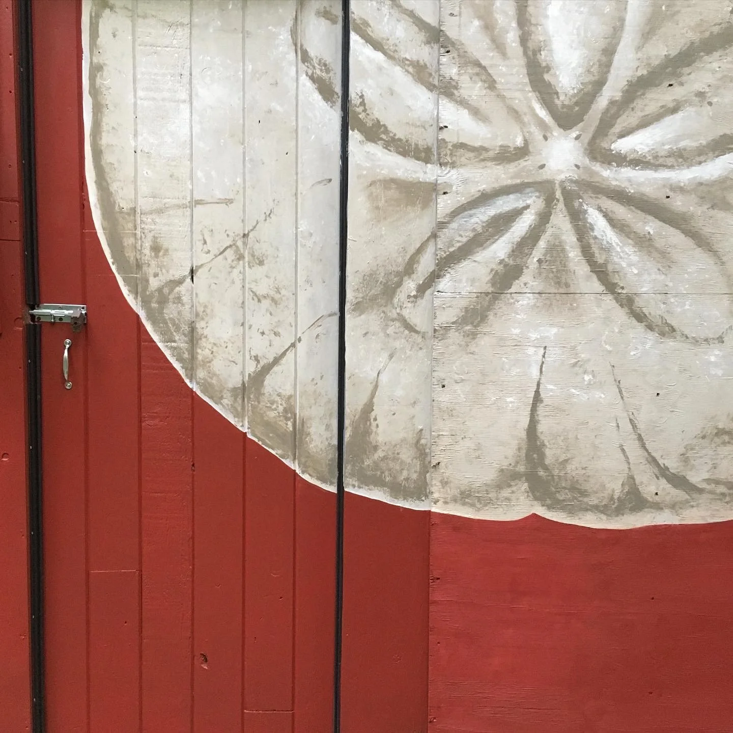 Un tableau mural avec un dessin de cercle partiel et de motifs rayonnants en nuances de gris, fixé sur un mur en bois peint en rouge.