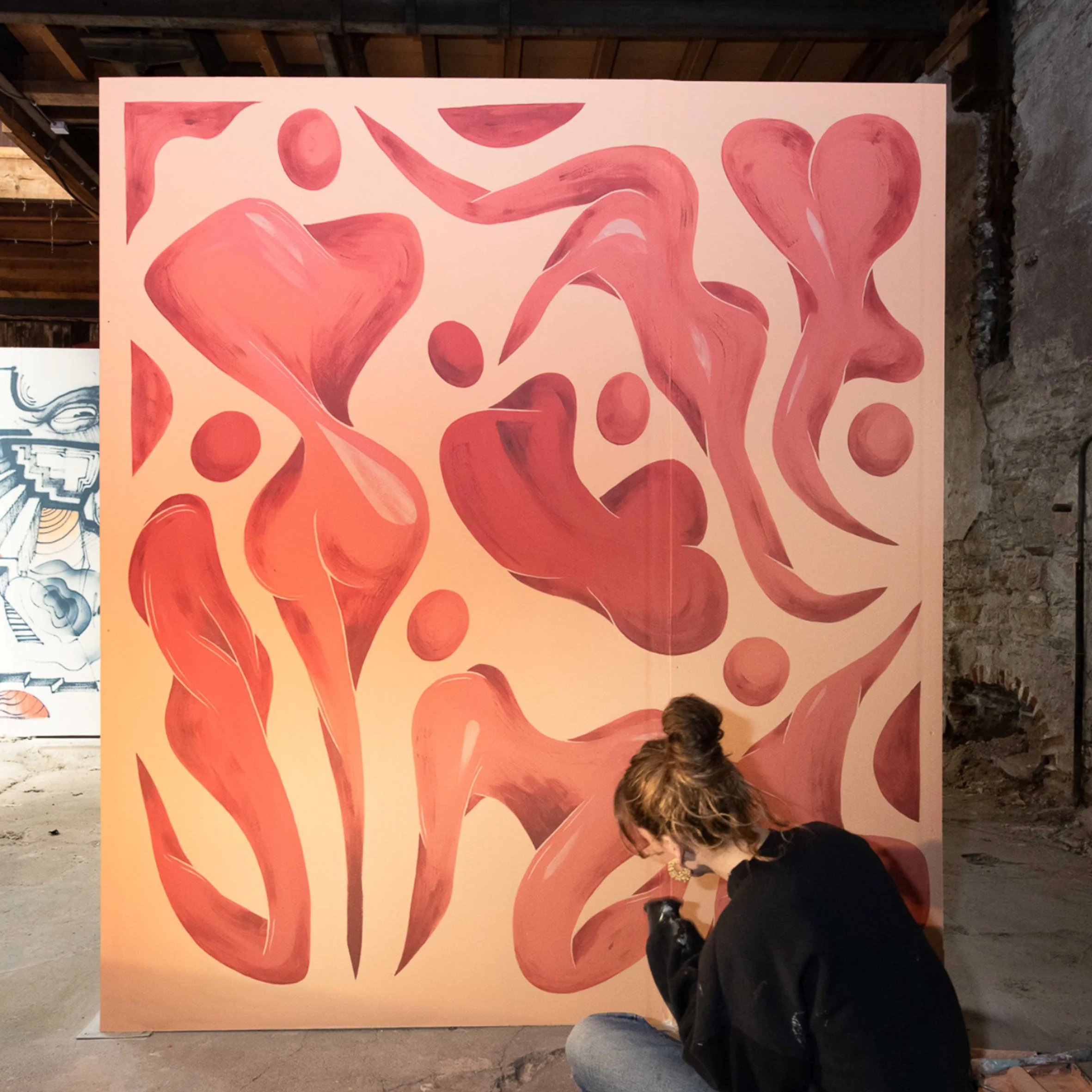 Une grande peinture abstraite avec des formes de cœurs roses sur un fond rose pâle exposée dans un espace d'art ou une galerie