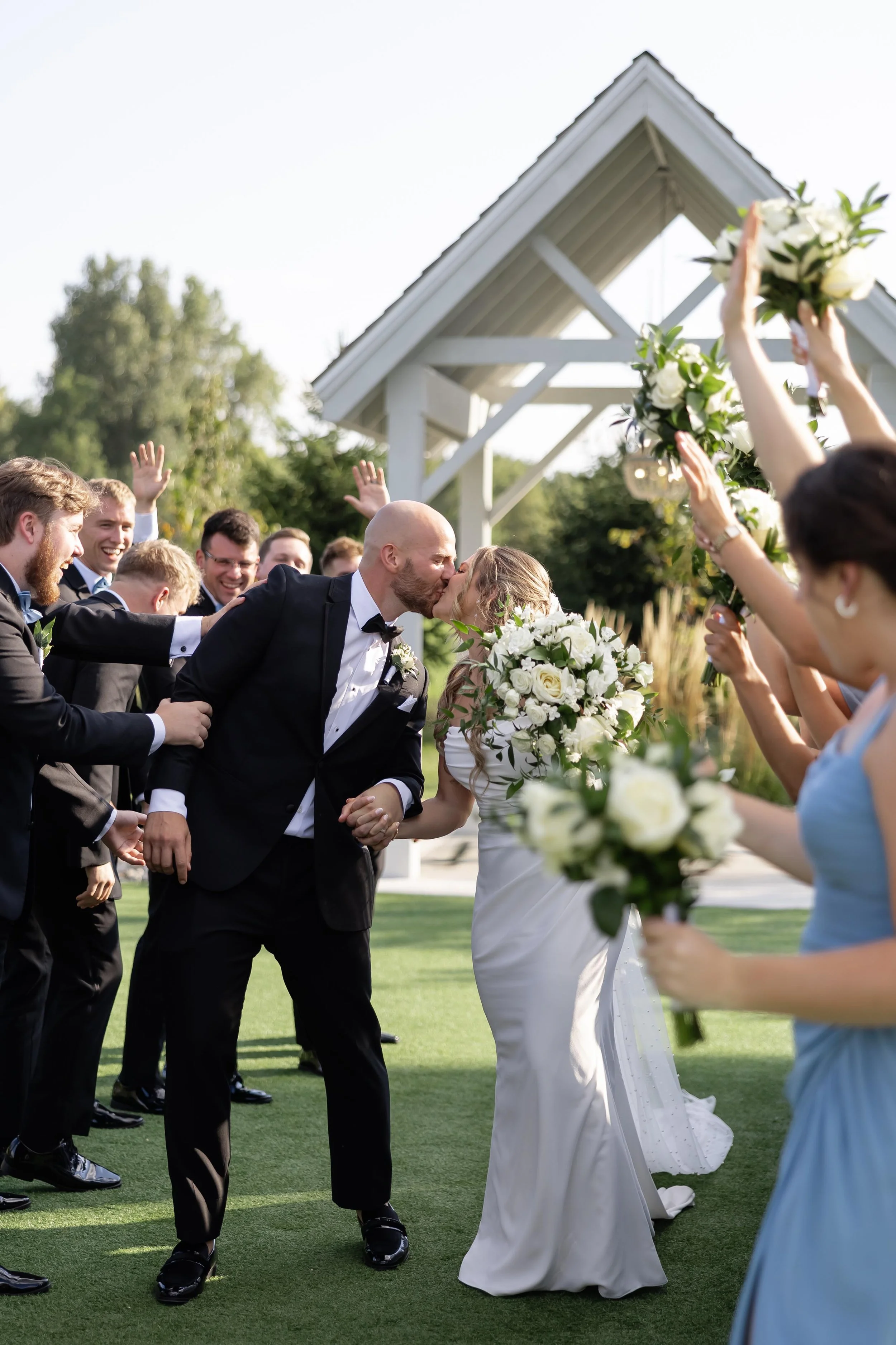 couple kissing as they walk up the aisle after their ceremony, with their bridal party and groom's men celebrating