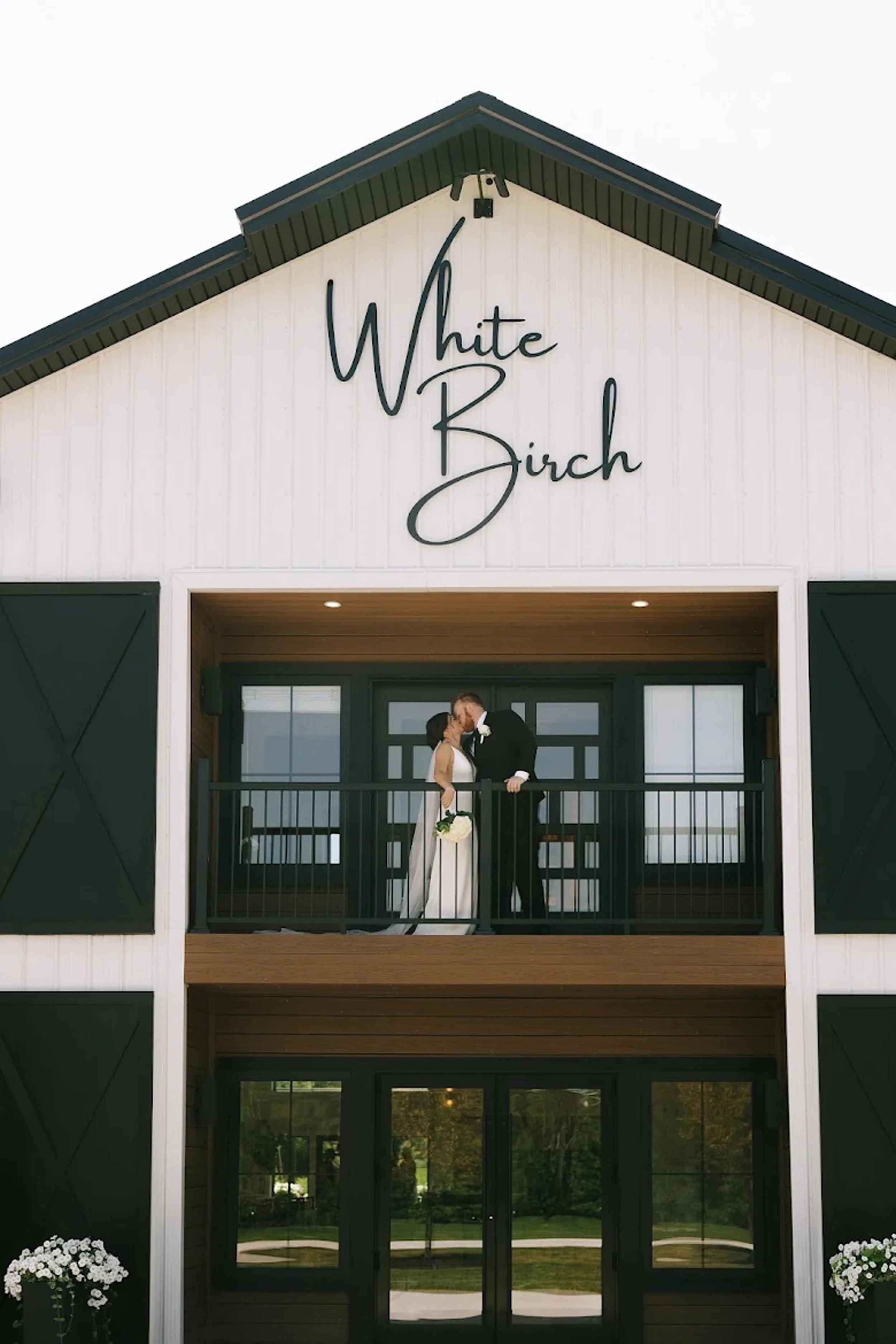 zoomed out shot of the front of the barn with a couple kissing on the balcny