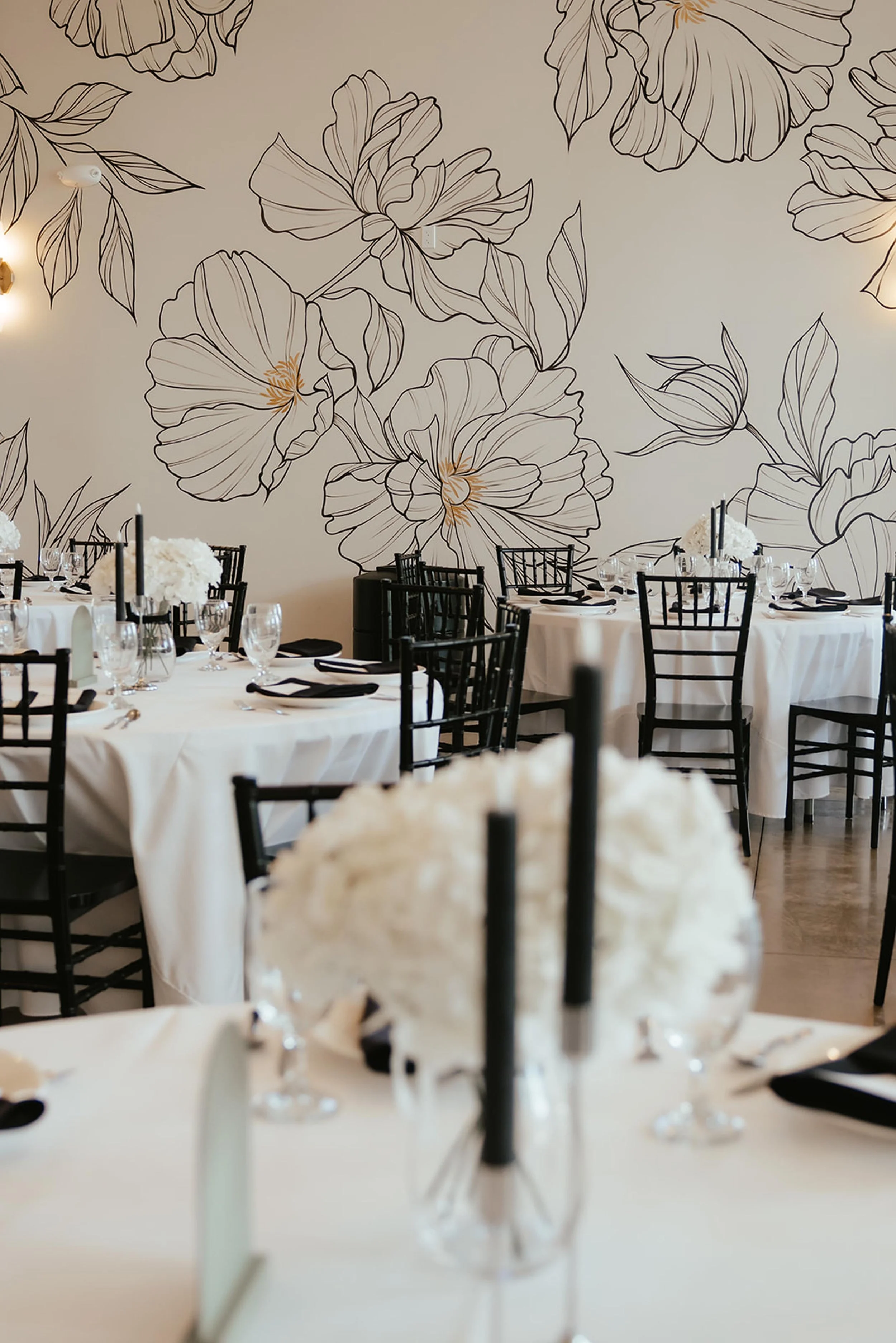 reception space with statement floral wallpaper, white tablecloths, and black chairs