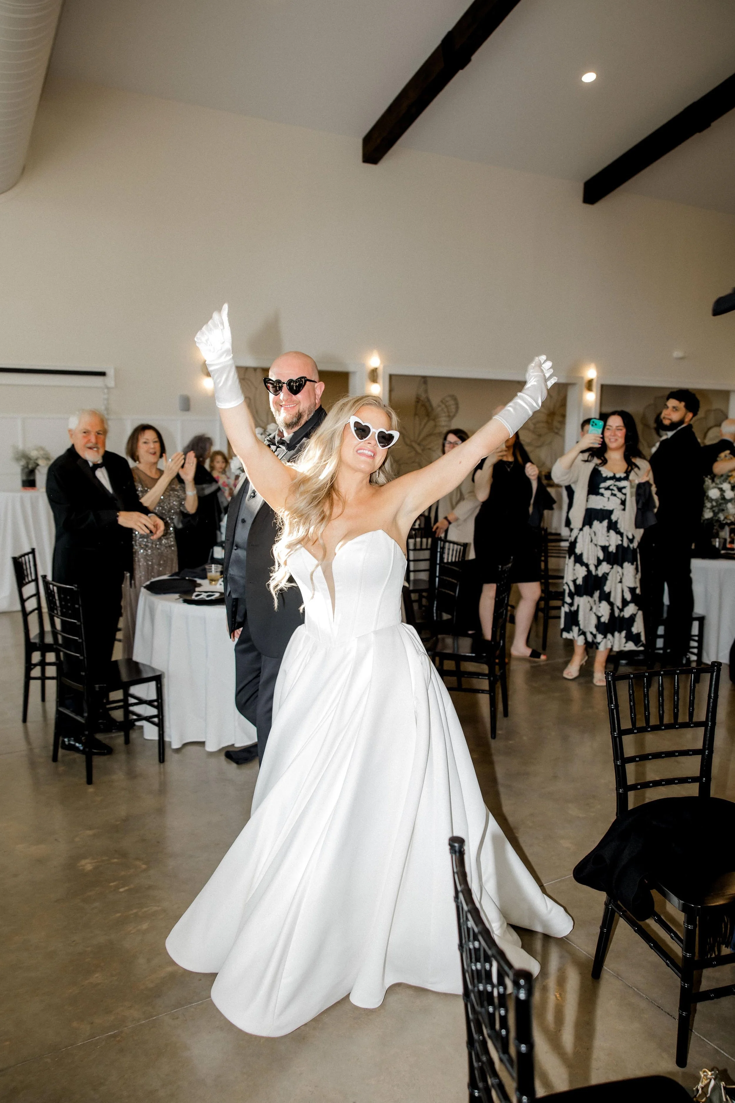 bride and groom walking into their reception with sunglasses and hands raised