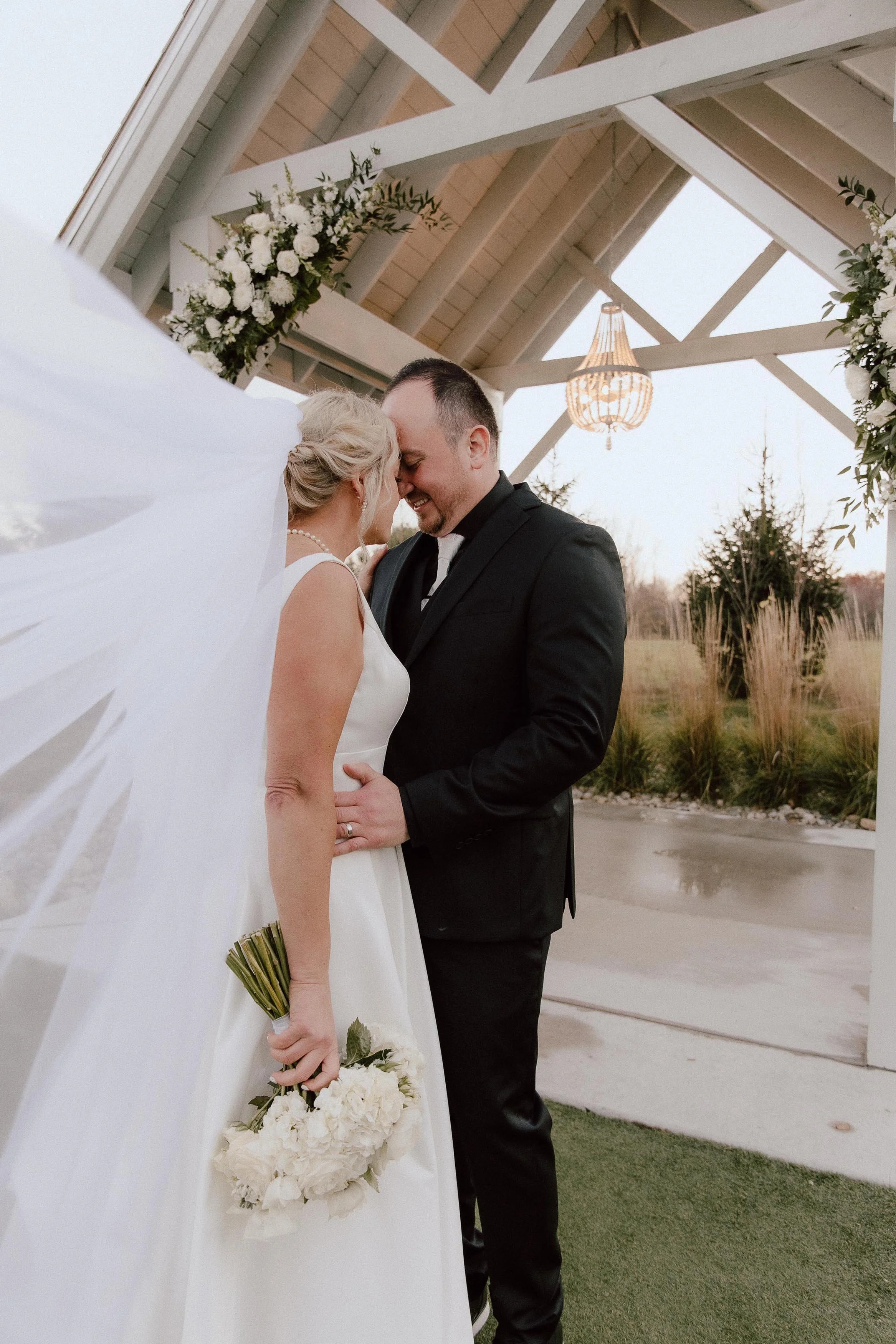couple embracing under the open-air chapel, with the bride's veil blowing in the wind