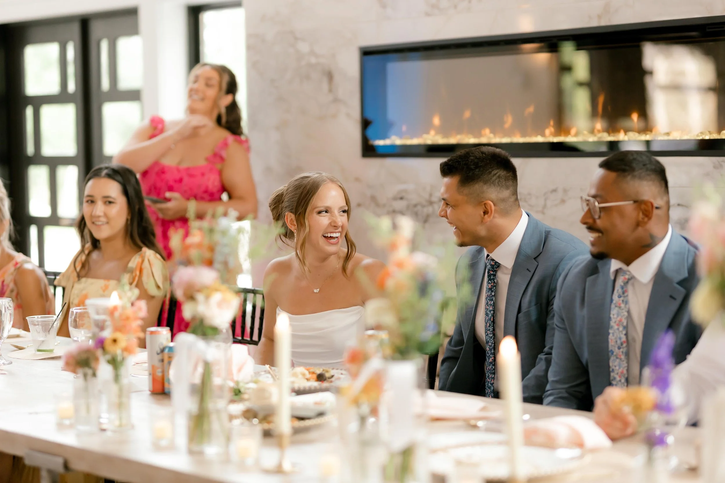 bride and grooms smiling at each other, sitting at the head table in front of the marble fireplace