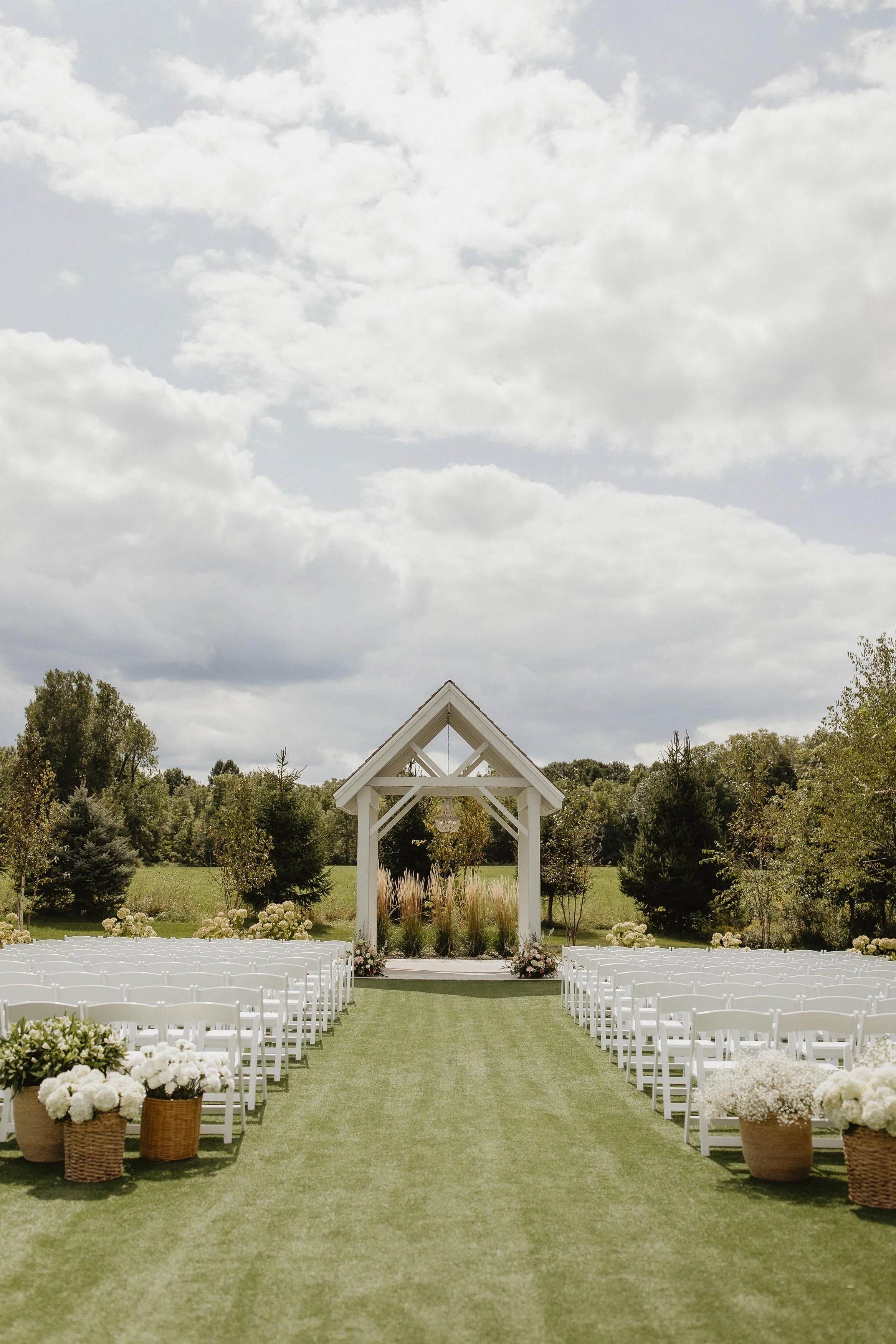 open-air chapel with white chairs set up for a wedding ceremony and many trees in the background