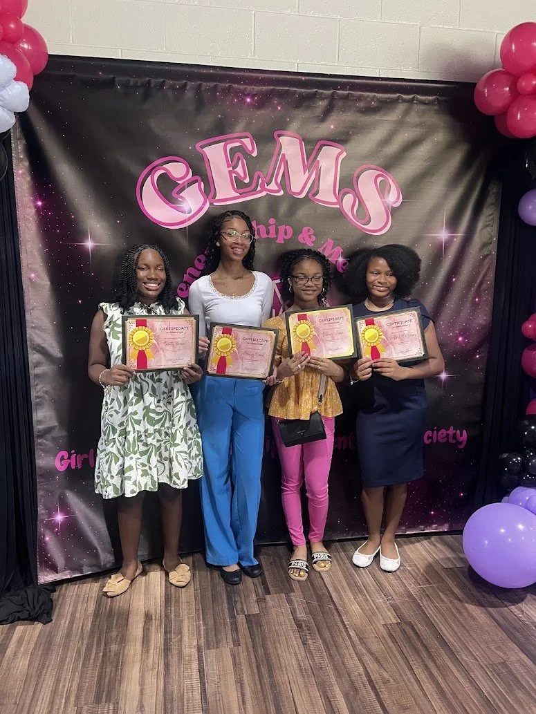 Four girls standing in front of a birthday backdrop holding certificates, celebrating with balloons on the sides.