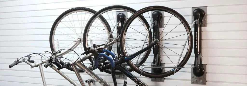 Bicycle wall rack with two bikes hanging upside down on a white slat wall.