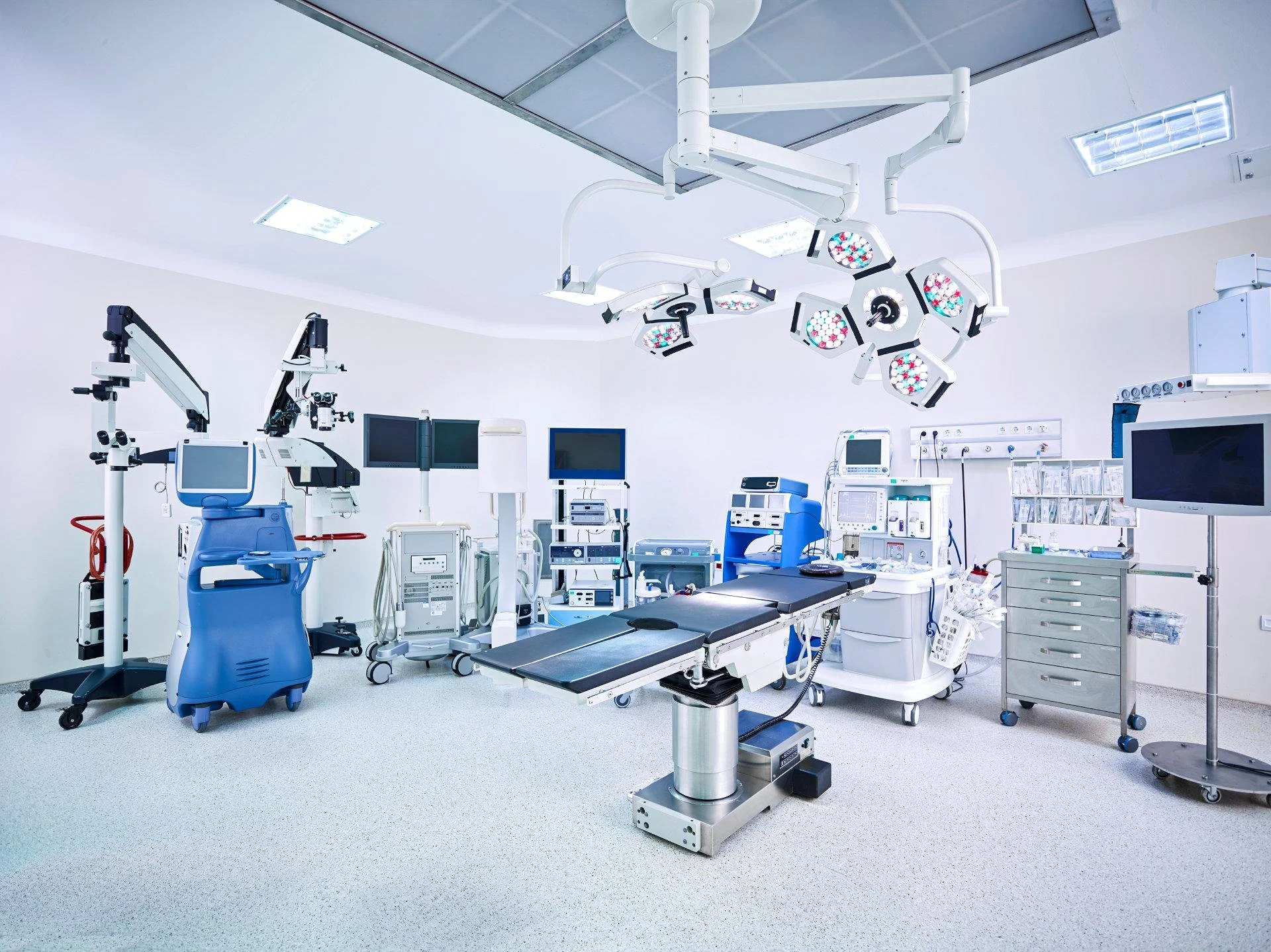 A modern, sterile operating room with surgical lights, medical monitors, and various medical equipment and supplies.