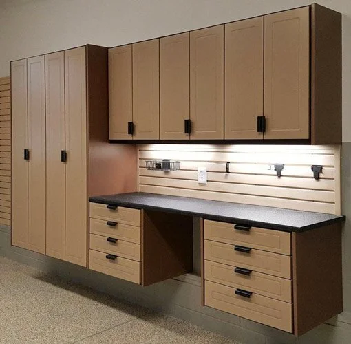 A workspace with wooden cabinets and drawers, a black countertop, and striped wall panels with hooks and power outlets.