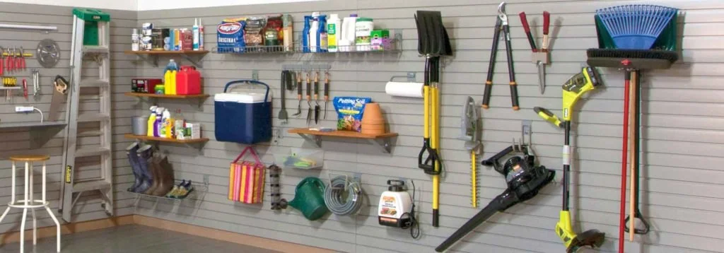 Garage wall with garden tools, shelves with paint and supplies, ladder, and boots.