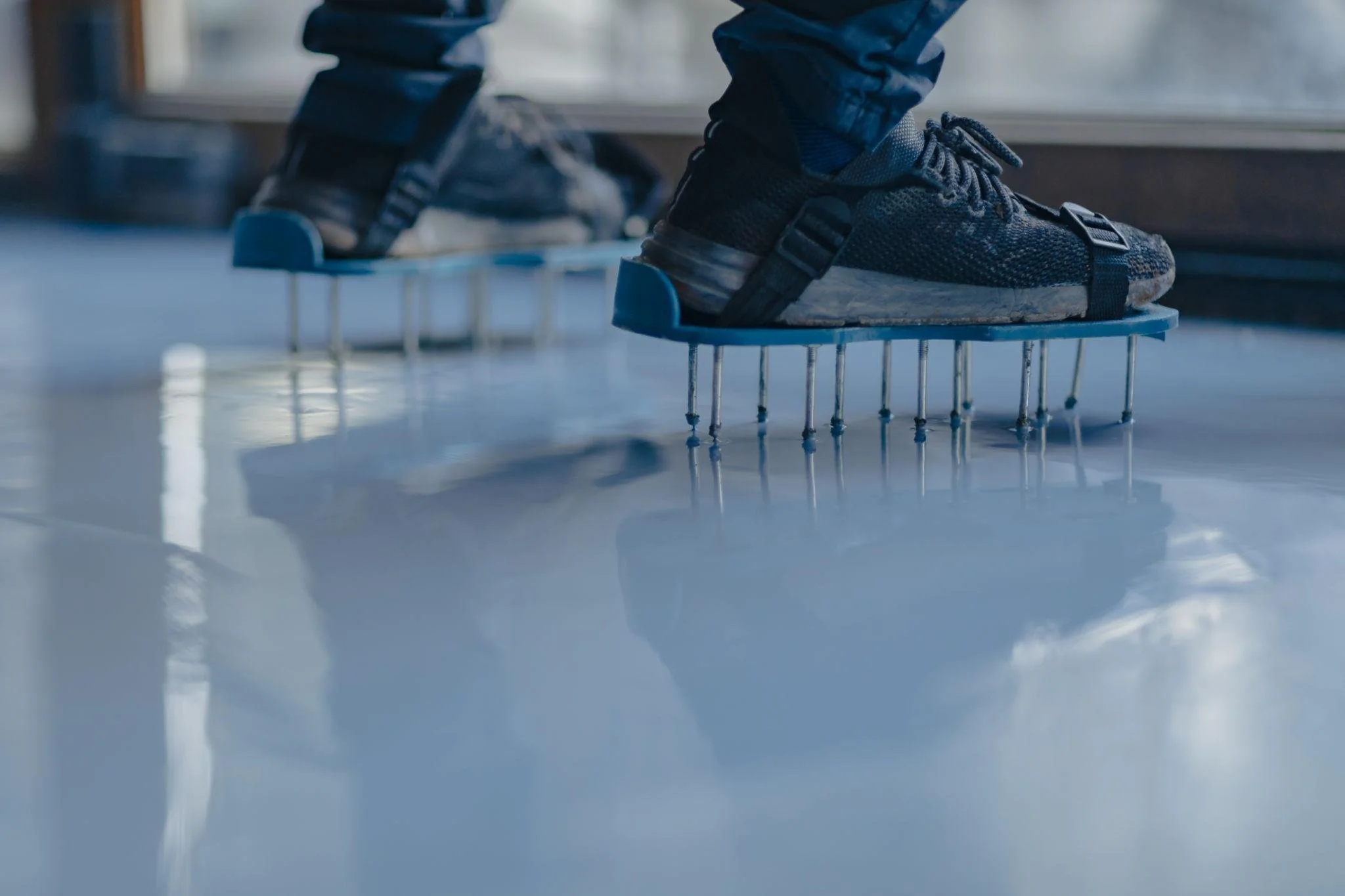 Close-up of black athletic shoes with propellers underneath, worn by person standing on a smooth, reflective surface by a window.
