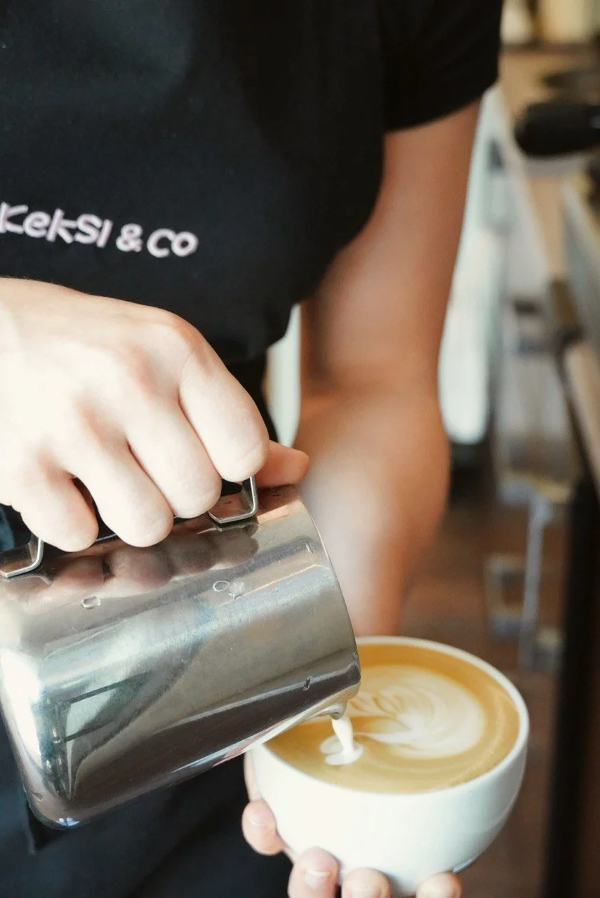 Barista pouring steamed milk into a cup of coffee, creating latte art.