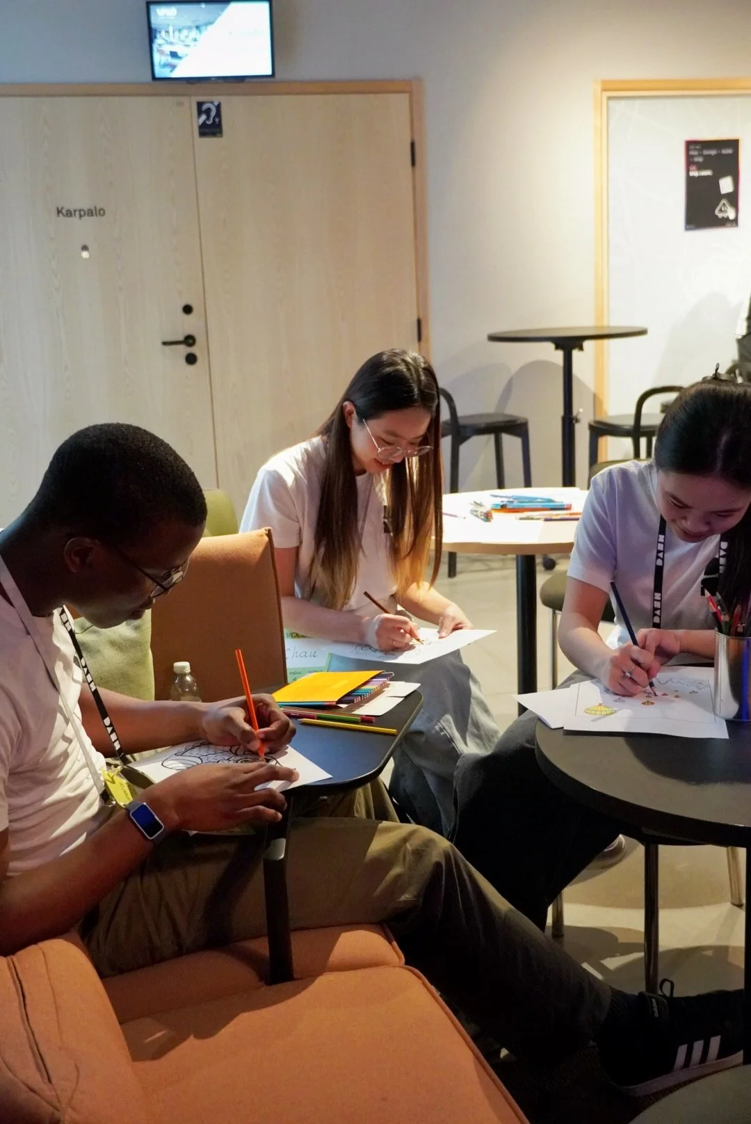 Three people sitting at a table coloring papers, with various coloring supplies scattered on the table.