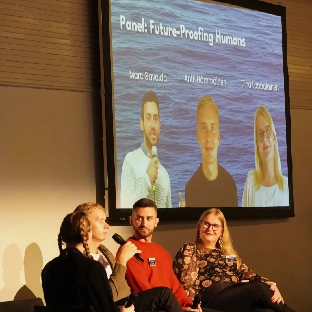 Panel discussion titled 'Future-Proofing Humans' showing three panelists, Marc Gavalda, Antti Hämmäinen, and Tiina Lappalainen, with a large screen behind them displaying their photos and names.
