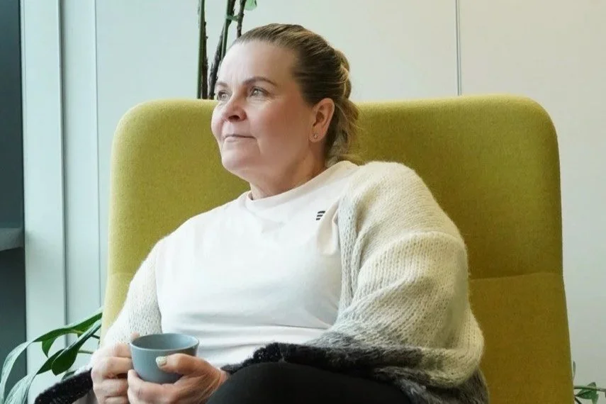 Woman sitting in a green armchair, holding a gray mug, looking thoughtfully out of frame. - Tanja Karonen - Nexpert - Photo by Symphony of views