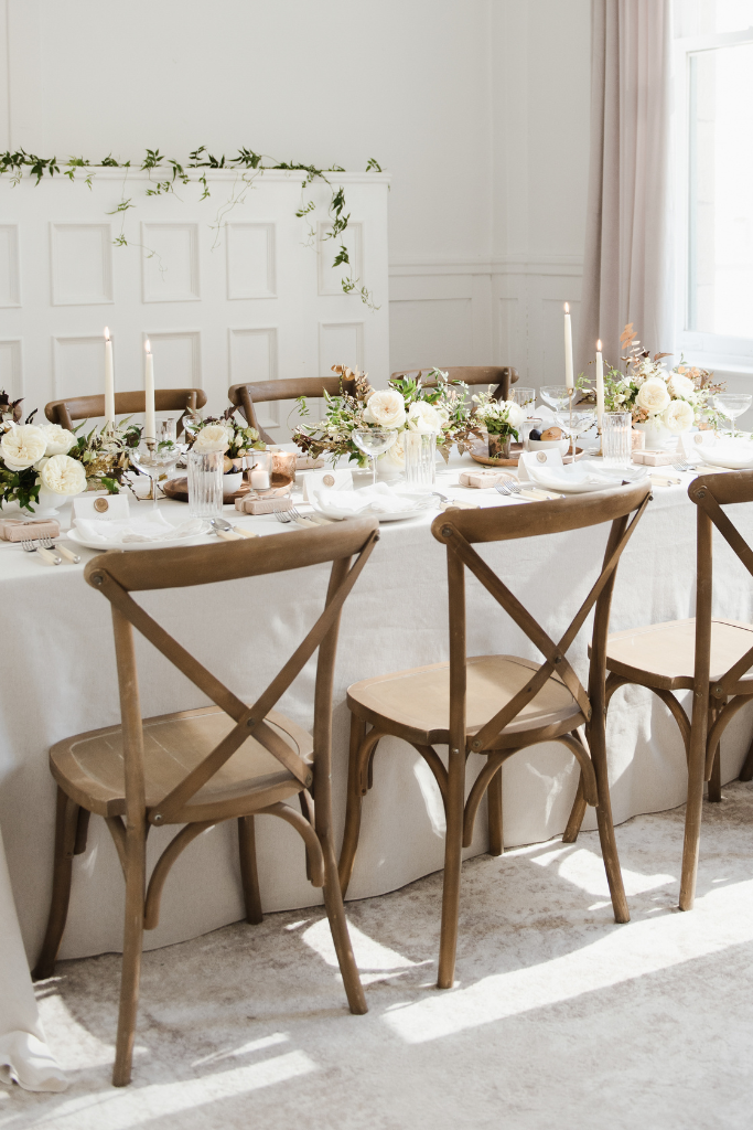 Une table décorée pour un repas, avec des fleurs blanches, des bougies et des vaisselles en cristal, dans une pièce lumineuse.