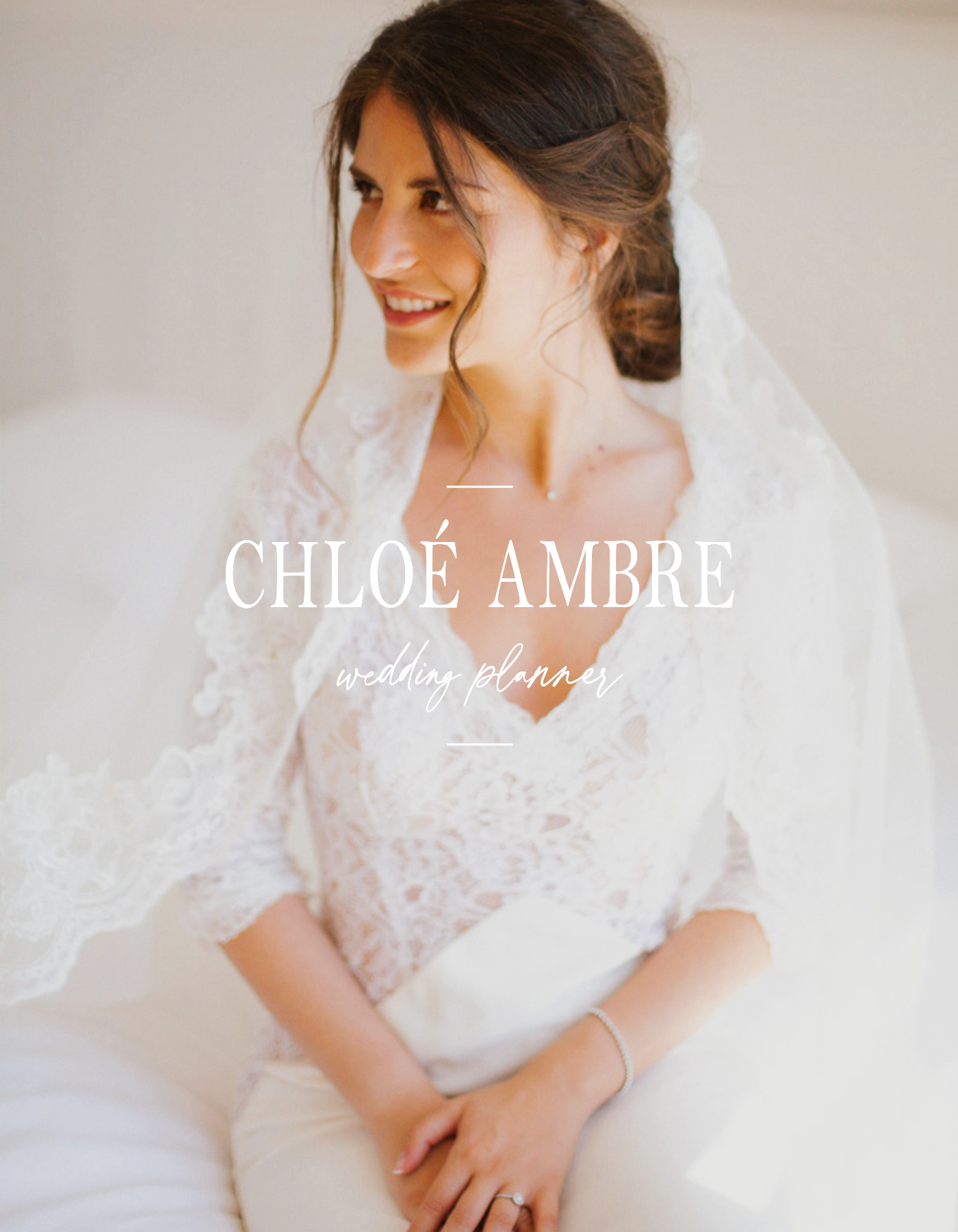 Une femme souriante en robe de mariage en dentelle, assise sur un canapé blanc, avec un bracelet à la main, portant un anneau, dans une ambiance lumineuse.