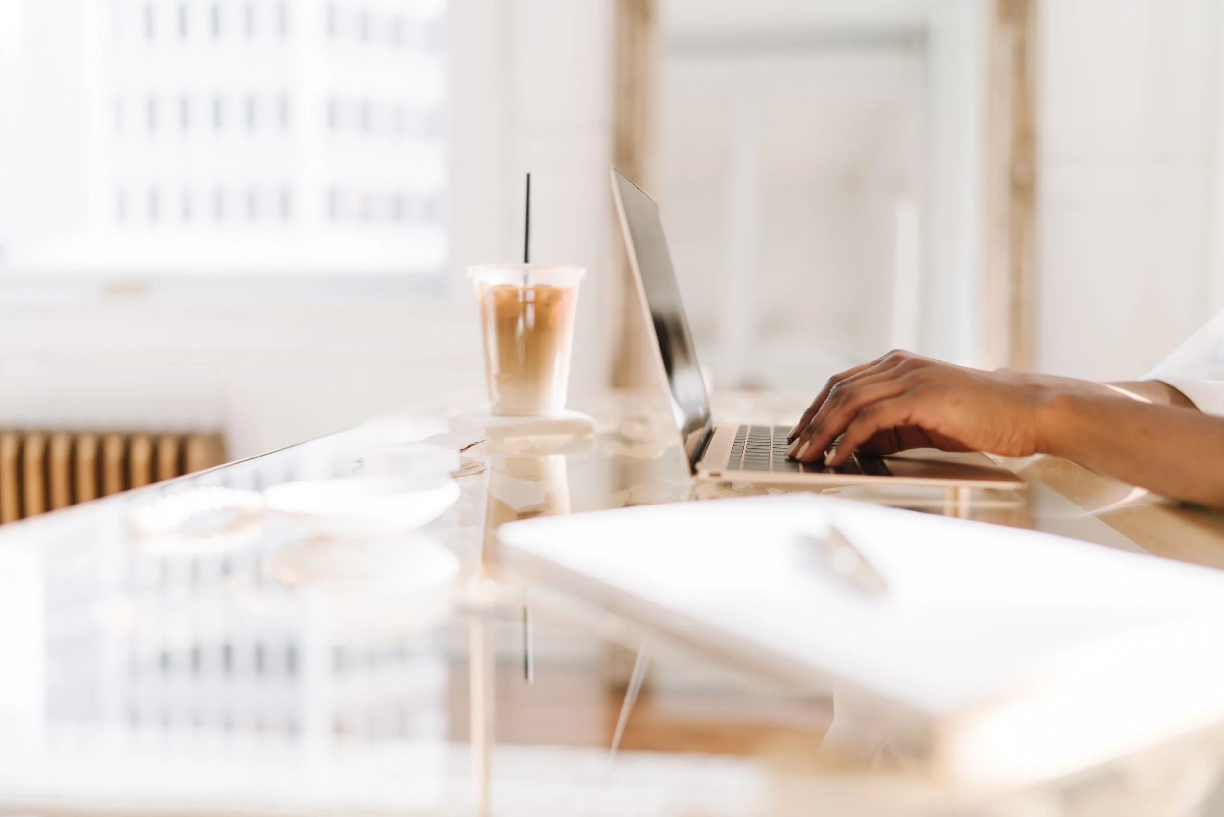 Une personne utilise un ordinateur portable sur une table en marbre, avec un café glacé à côté dans un environnement lumineux, probablement un café ou un espace de travail domestique.