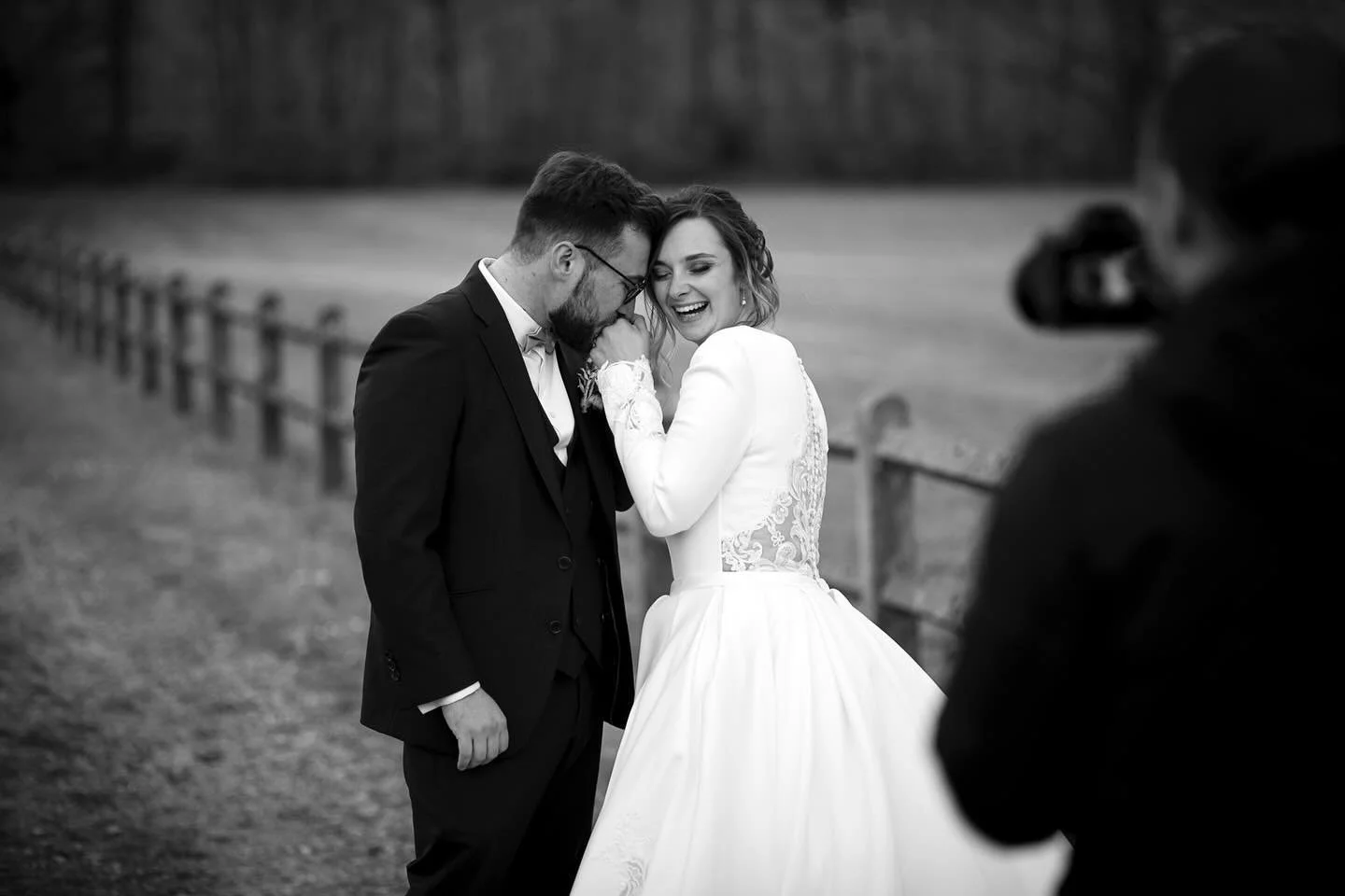 Un couple de mariés en noir et blanc lors d'une séance photo de mariage, la femme en robe blanche et l'homme en costume, souriant et partageant un moment intime dans un extérieur