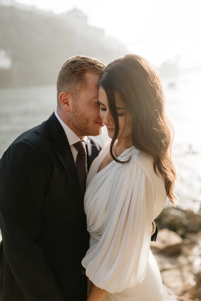 Un couple qui se tient près de la mer, en tenue de mariage, partage un moment intime et heureux.