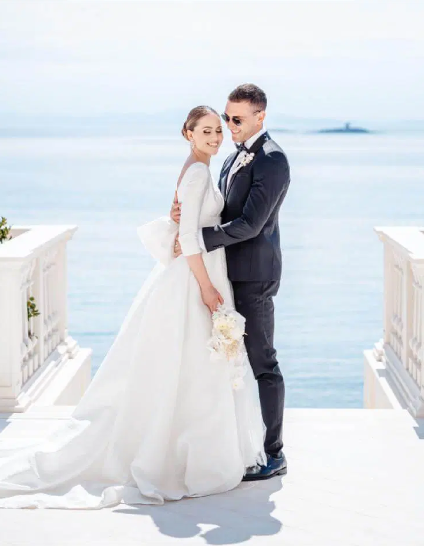 Un couple de mariés en costume et robe de mariage souriant, posant près de la mer lors de leur mariage en plein air.