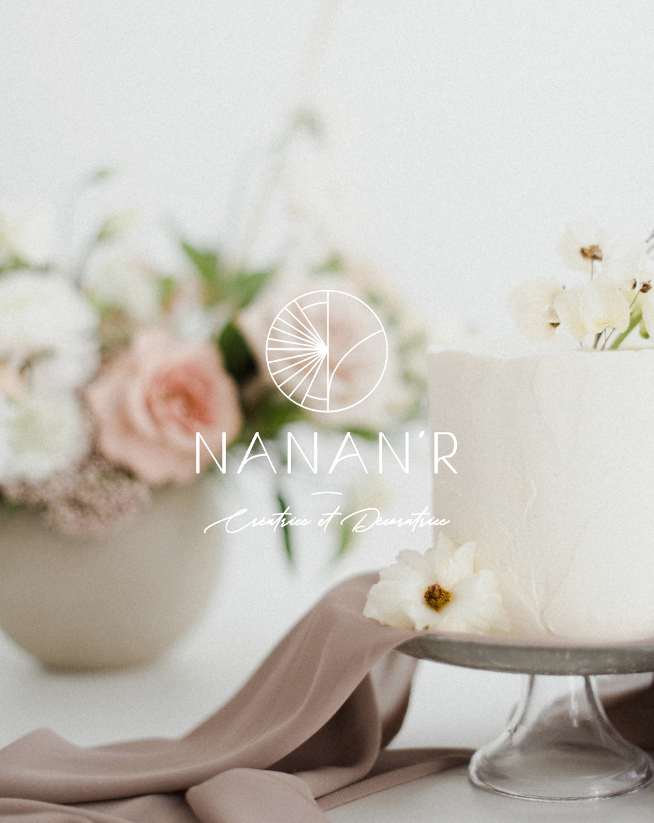 Gâteau blanc décoré avec des fleurs blanches et crème, avec un bouquet de fleurs pastel derrière.