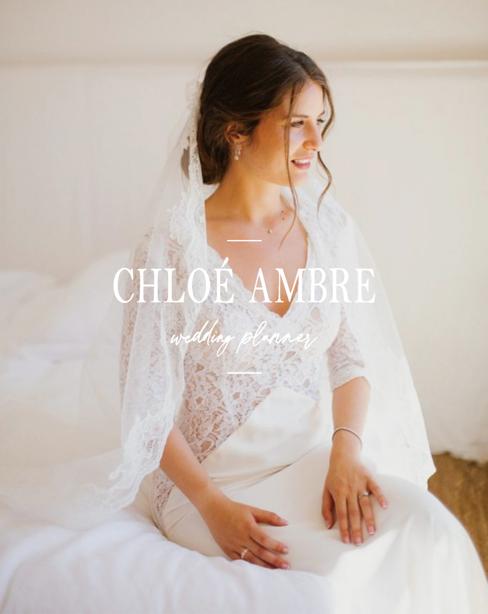 Une femme en robe de mariée assise sur un lit blanc, regardant à droite, avec du maquillage léger et des cheveux bruns ondulés. Sur l'image est écrit : 'Chloé Ambre, wedding planner'.
