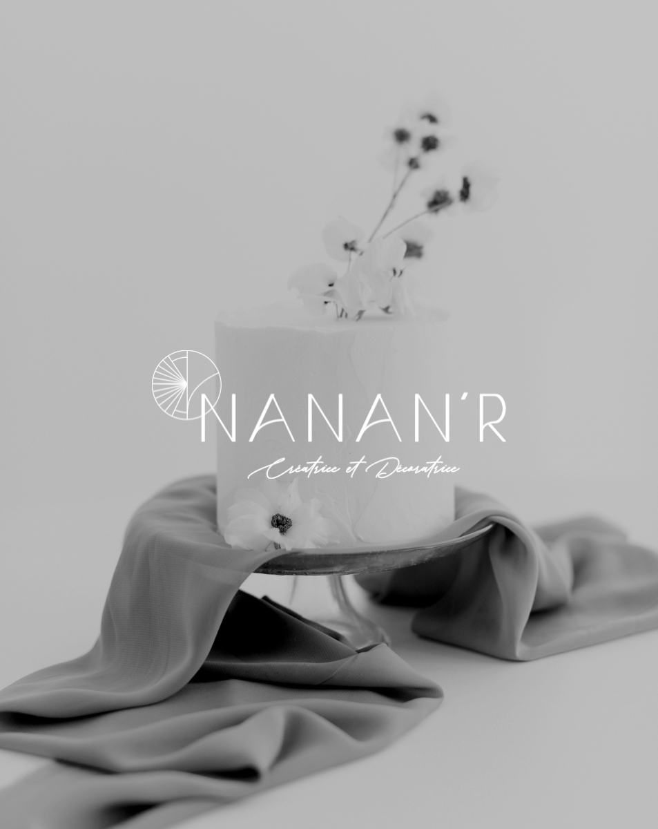 Un gâteau blanc orné de fleurs séchées, posé sur une surface recouverte de tissu fluide, avec le texte "NANAN'R Créatrice et Decoratrice"