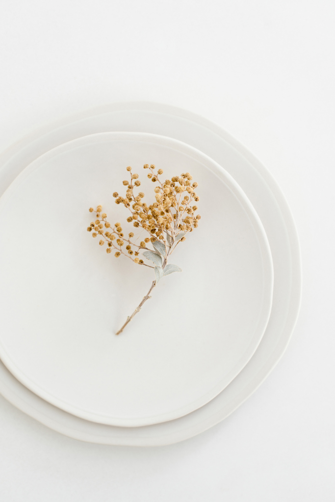 Une petite branche de fleurs séchées sur une assiette blanche.