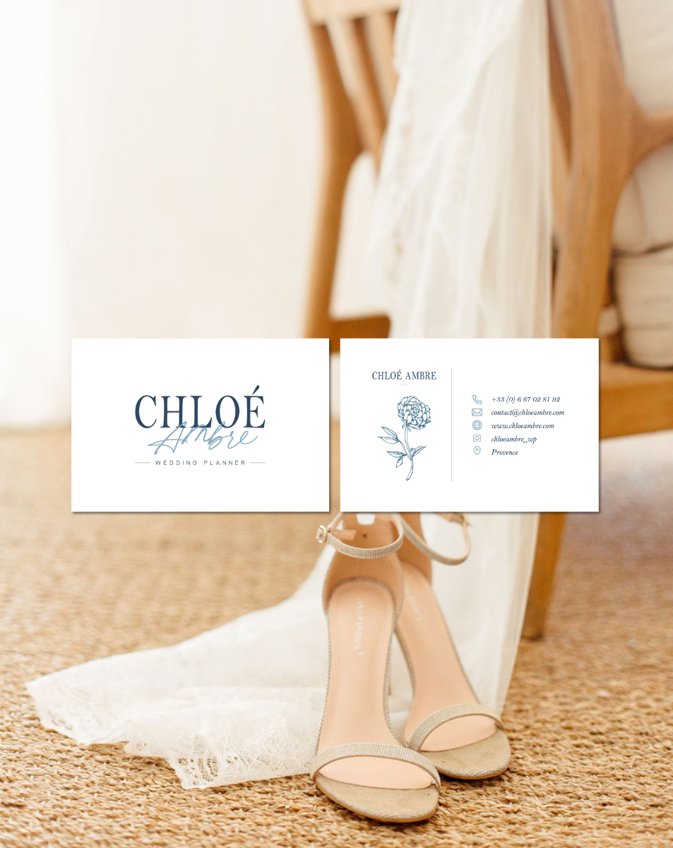 Cartes de visite pour un organisateur de mariage, posées devant une robe de mariée et une paire de chaussures à talons, avec un fond de sol en tapis de jute.
