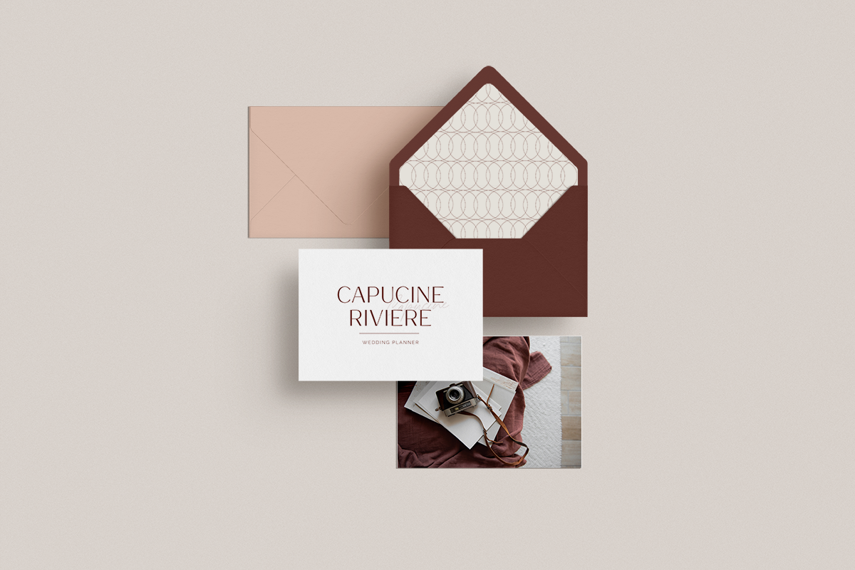 Une enveloppe marron, une carte de visite avec le texte "Capucine Riviere Wedding Planner", une photo avec un appareil photo vintage et des livres, et une autre enveloppe beige sur un fond clair.