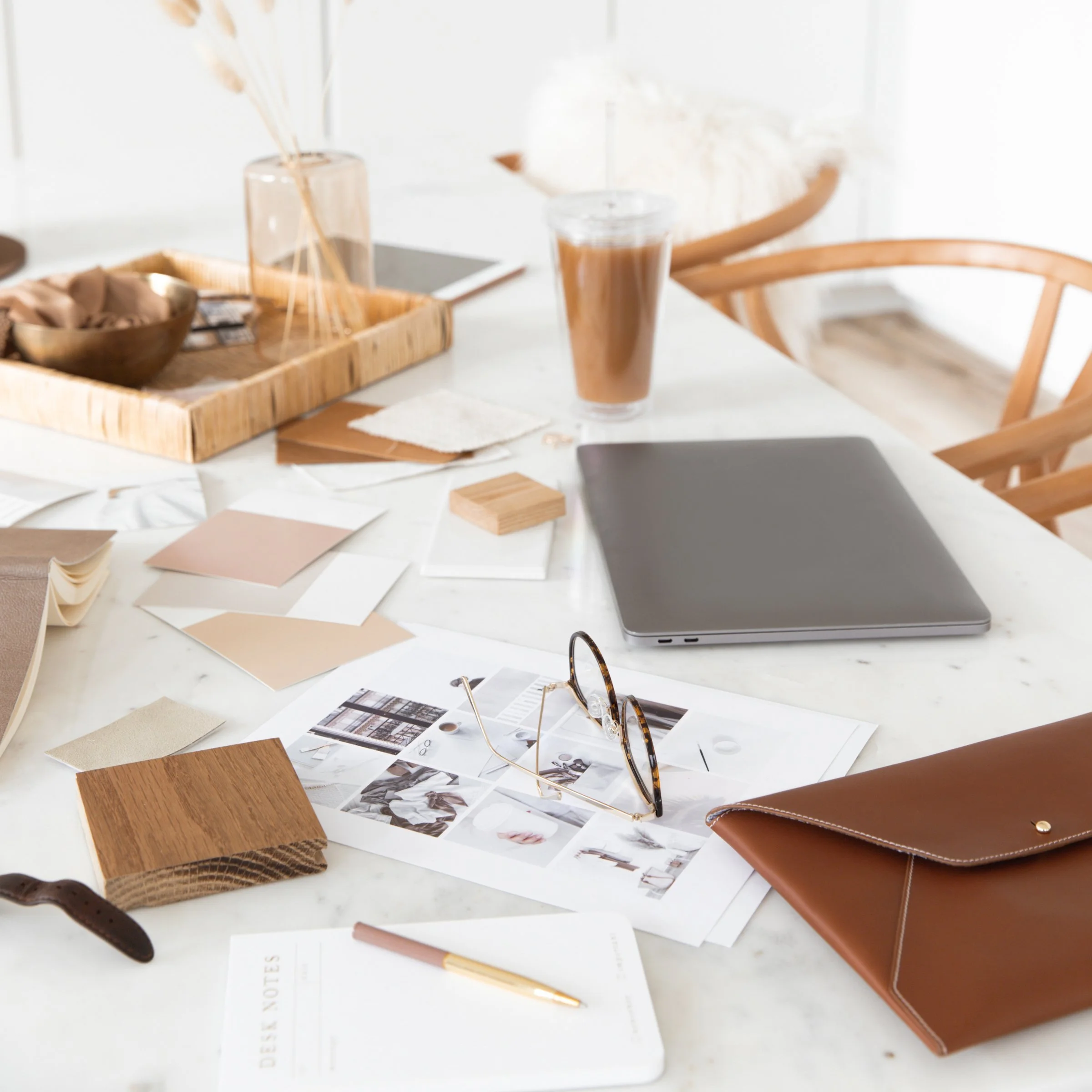 Un bureau avec divers échantillons de matériaux, des papiers, un ordinateur portable, une paire de lunettes et d'autres objets de travail créatif.