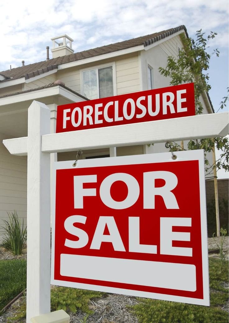 A house with a 'Foreclosure' sign on top and a 'For Sale' sign below, indicating the property is for sale due to foreclosure.