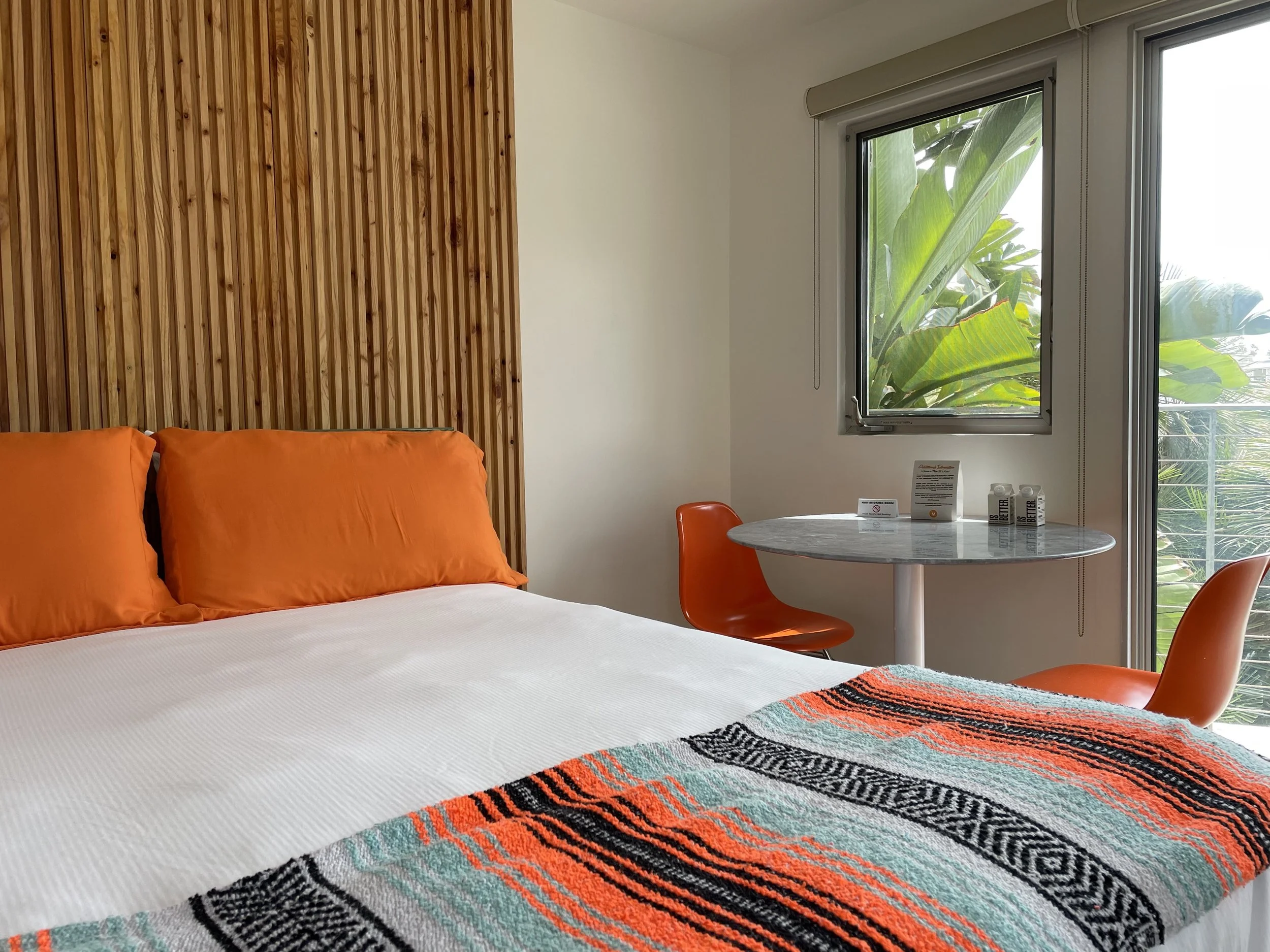 Tiki Vista room with queen bed, orange pillows, Mexican blanket and private balcony at The Malibu Motel, Malibu California