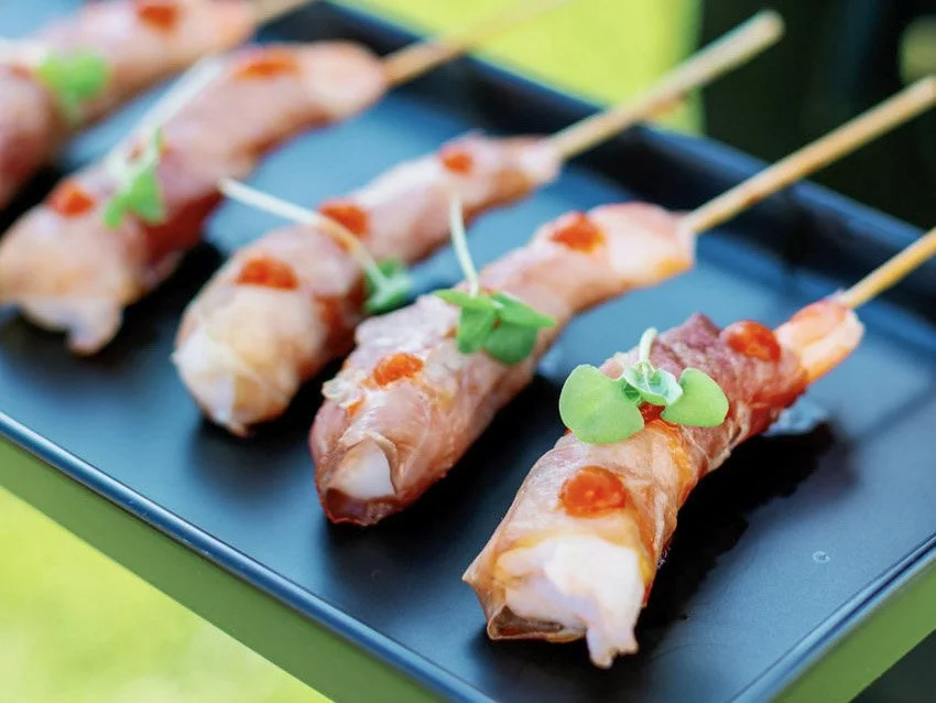 Skewered shrimp appetizers garnished with microgreens on a black rectangular plate. California Central Coast Chefs gourmet bites and tastings included.