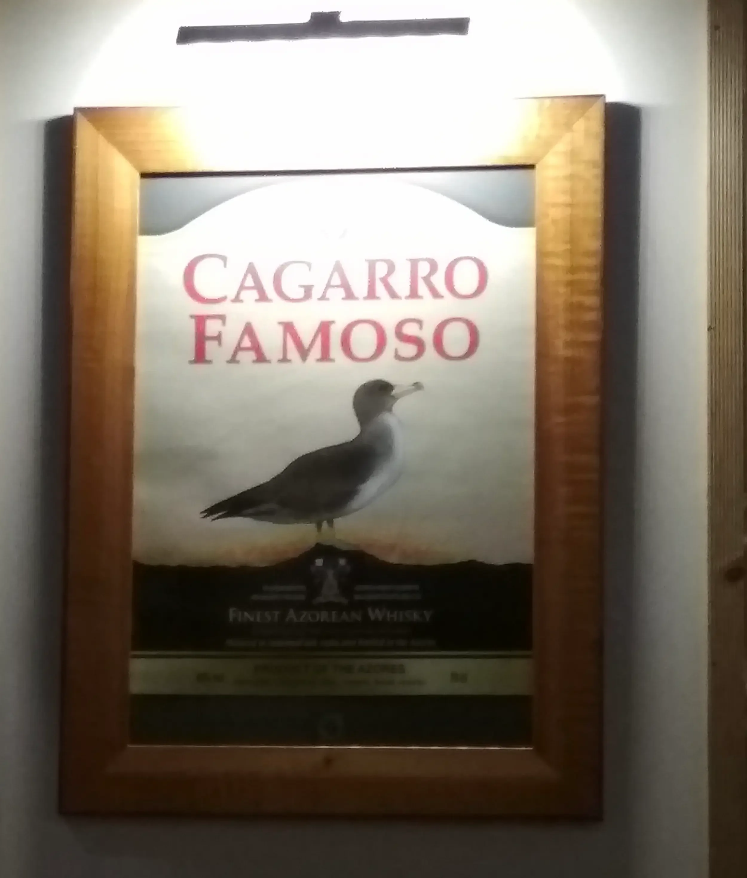 “Cagarro Famoso” advertising poster in a bar in the Azores, parodying a well-known whisky brand through a humorous local reference.