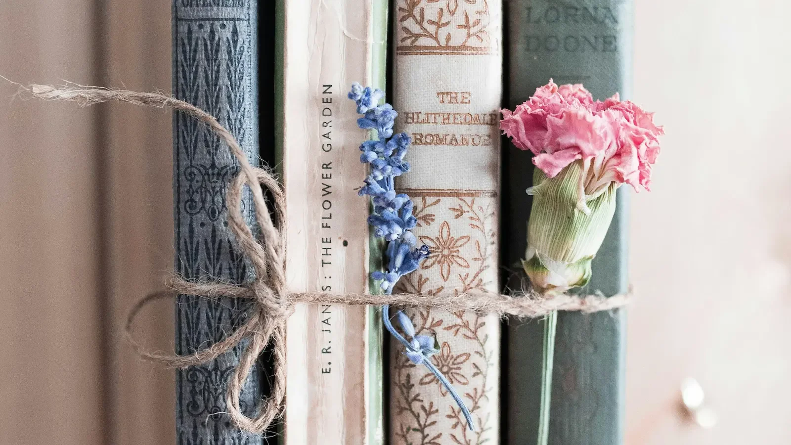 Four vintage books in soft pastel tones tied with twine, with a sprig of lavender and a dried carnation