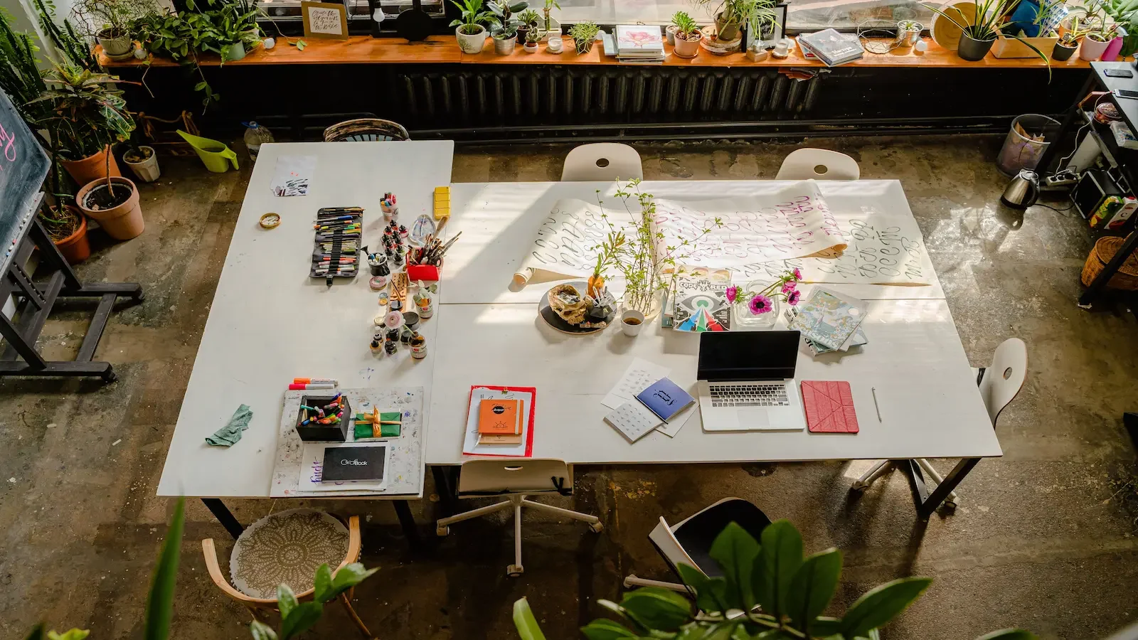 Wide view of a laptop workspace on a long desk in a colourful office with floral decorations