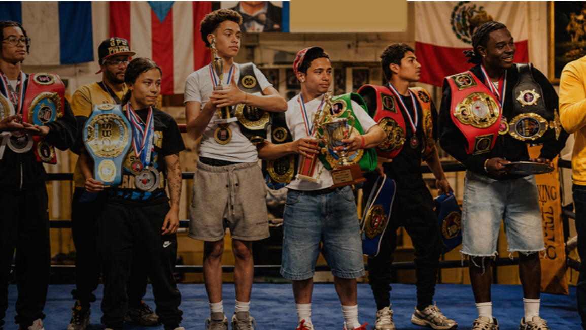 Boxers on the podium receiving awards at a boxing event, holding trophies and wearing championship belts.