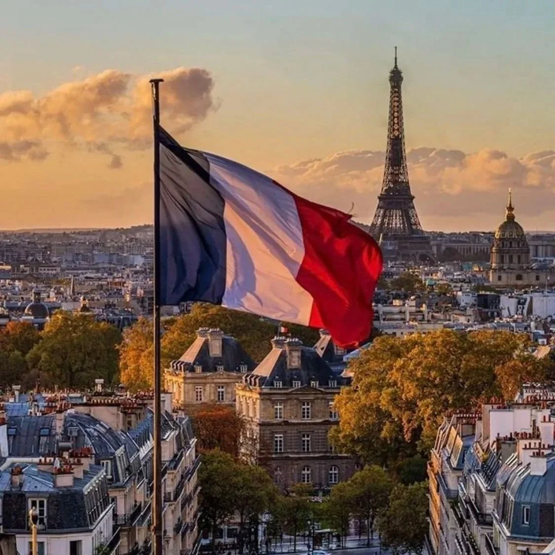 La bandera de Francia ondeando con la Torre Eiffel al fondo en París al atardecer.