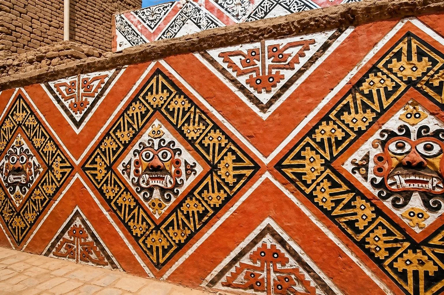Pared decorativa con patrones tradicionales coloridos y máscaras en relieve, mostrando arte indígena.