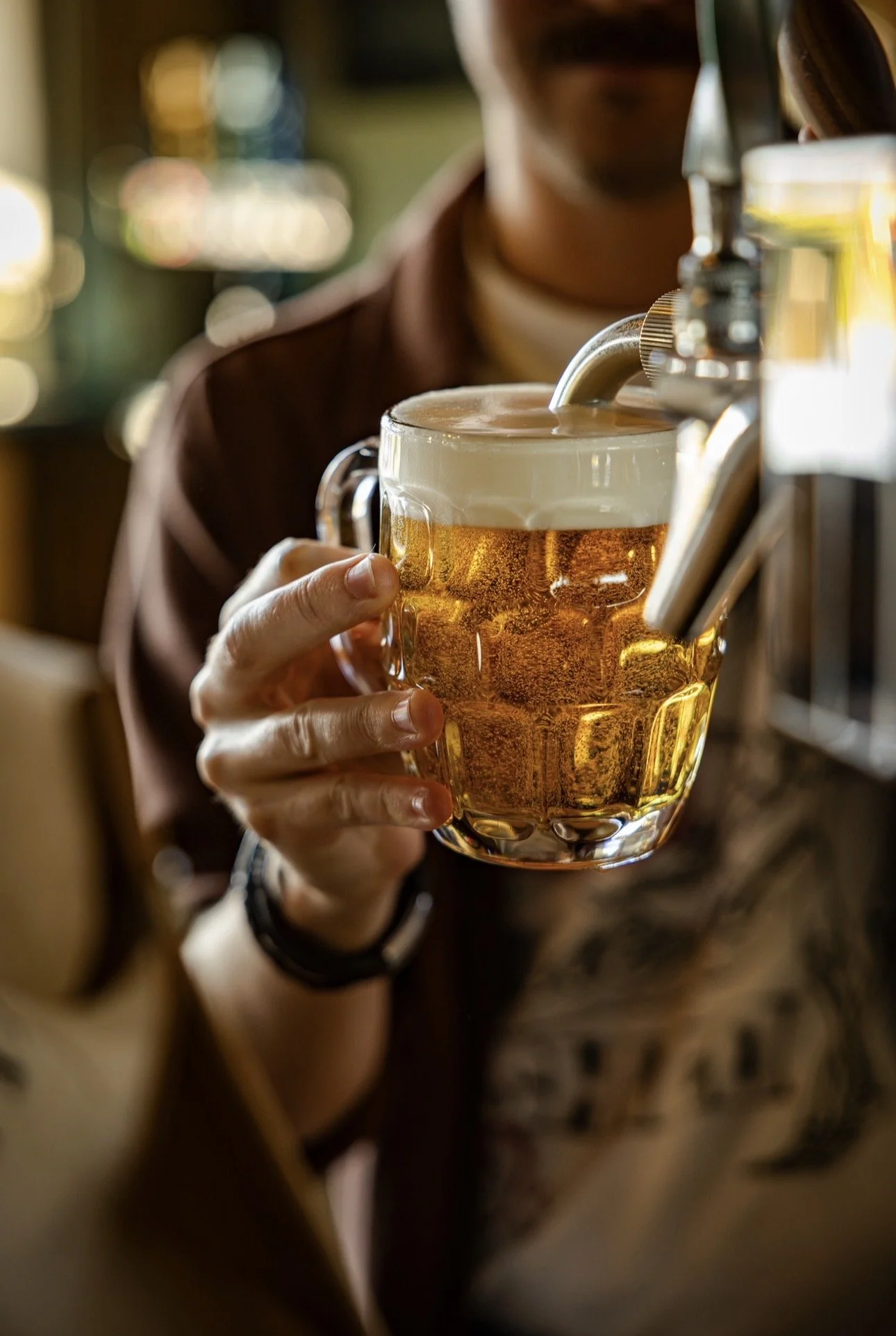 A person pouring beer from a tap into a glass mug at a bar or pub.