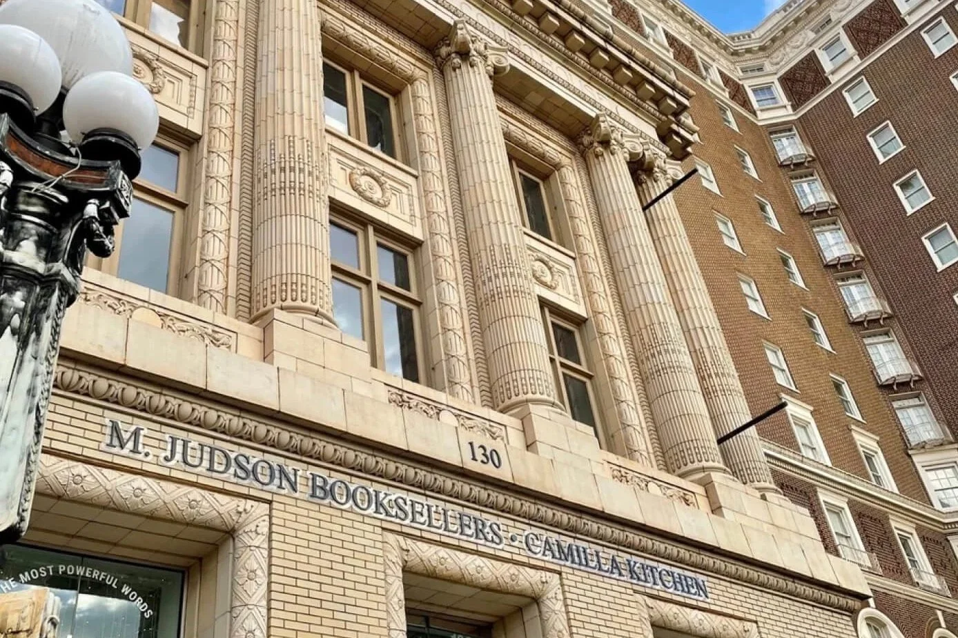 Exterior view of a historic building with ornate architectural details and large windows, featuring a sign for M. Judson Booksealers and Camelia Kitchen above the entrance, with a street lamp in the foreground.