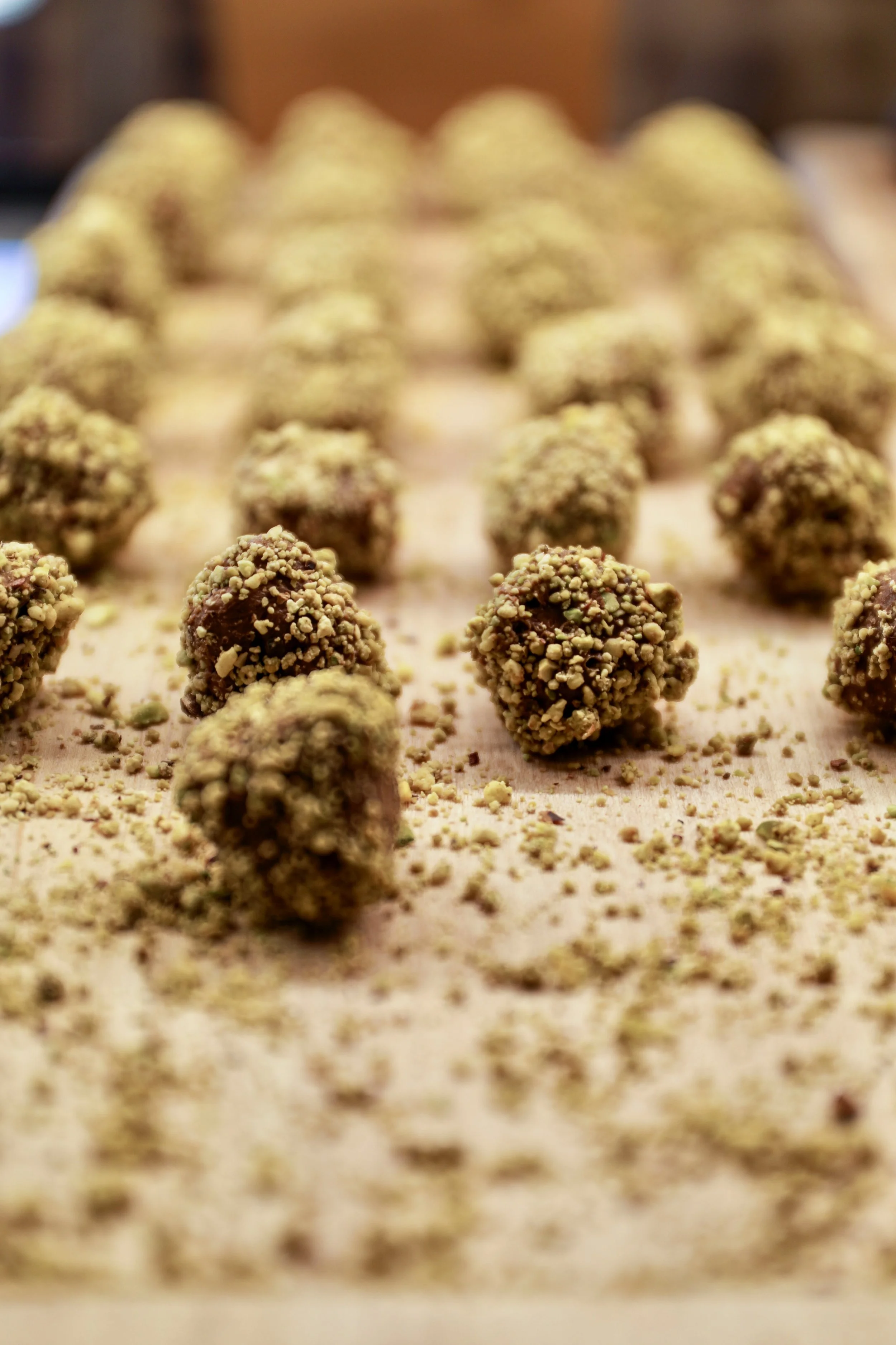 Close-up of chocolate truffles covered with chopped nuts, arranged on a flat surface with scattered crumbs.