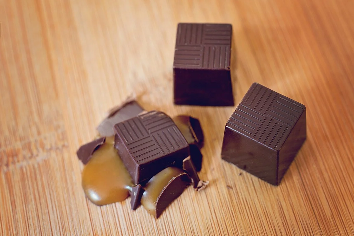 Two cubes of dark chocolate and broken piece with caramel on a wooden surface.