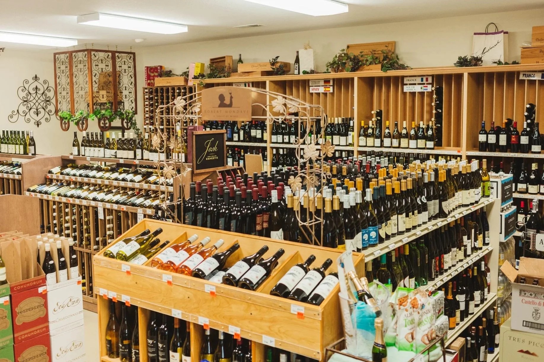 A wine store aisle with shelves filled with various bottles of wine, organized by type and country, with decorative elements and a wooden wine rack.