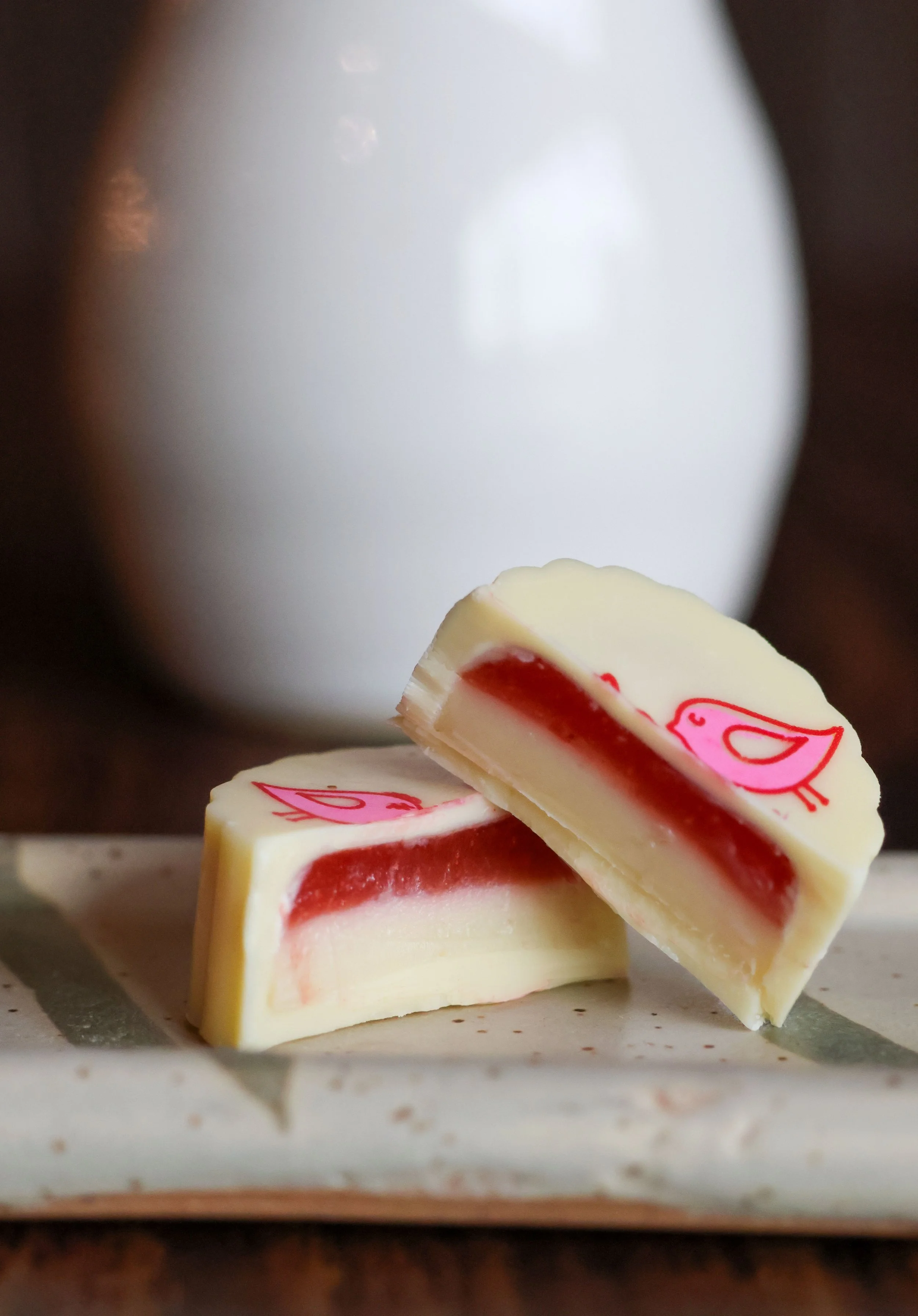 Pieces of white and red layered chocolate with pink bird design on top, placed on a piece of parchment paper.