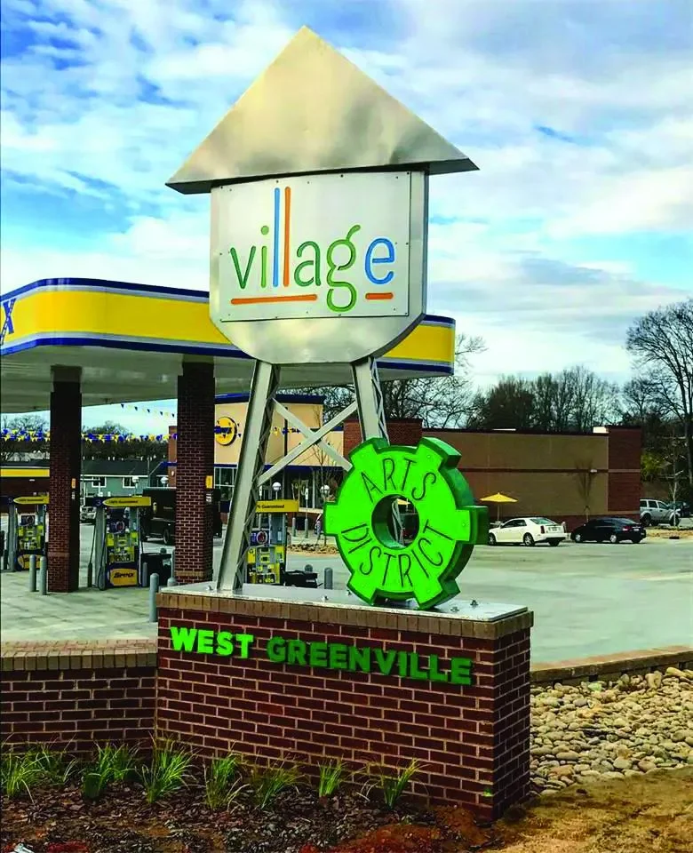 Sign for West Greenville with the words 'Village' in colorful letters, and a green gear-shaped sign with 'Arts District' in black letters.