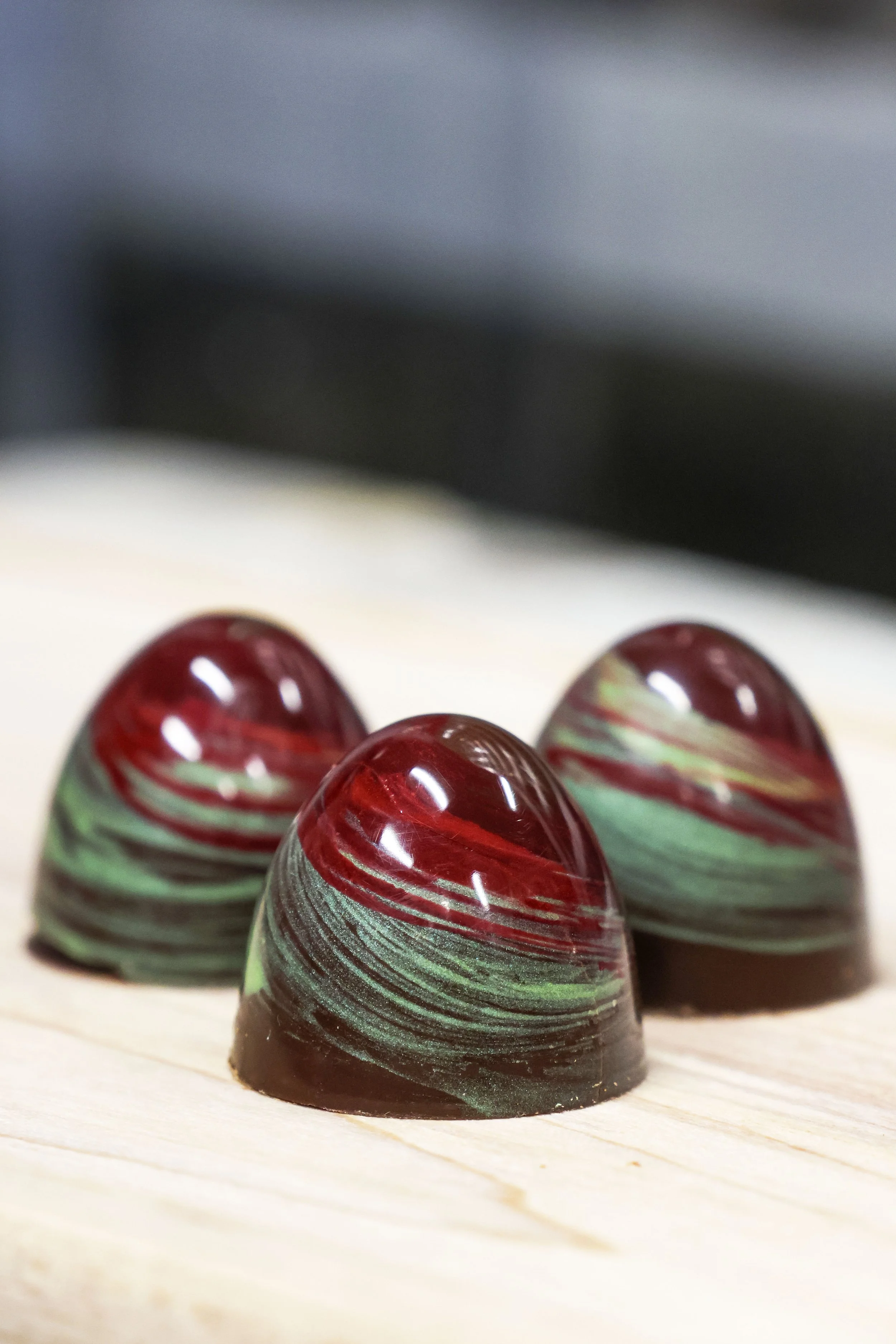 Close-up of colorful, marble-patterned chocolate bonbons with swirls of red, green, and white, arranged on a light wooden surface.