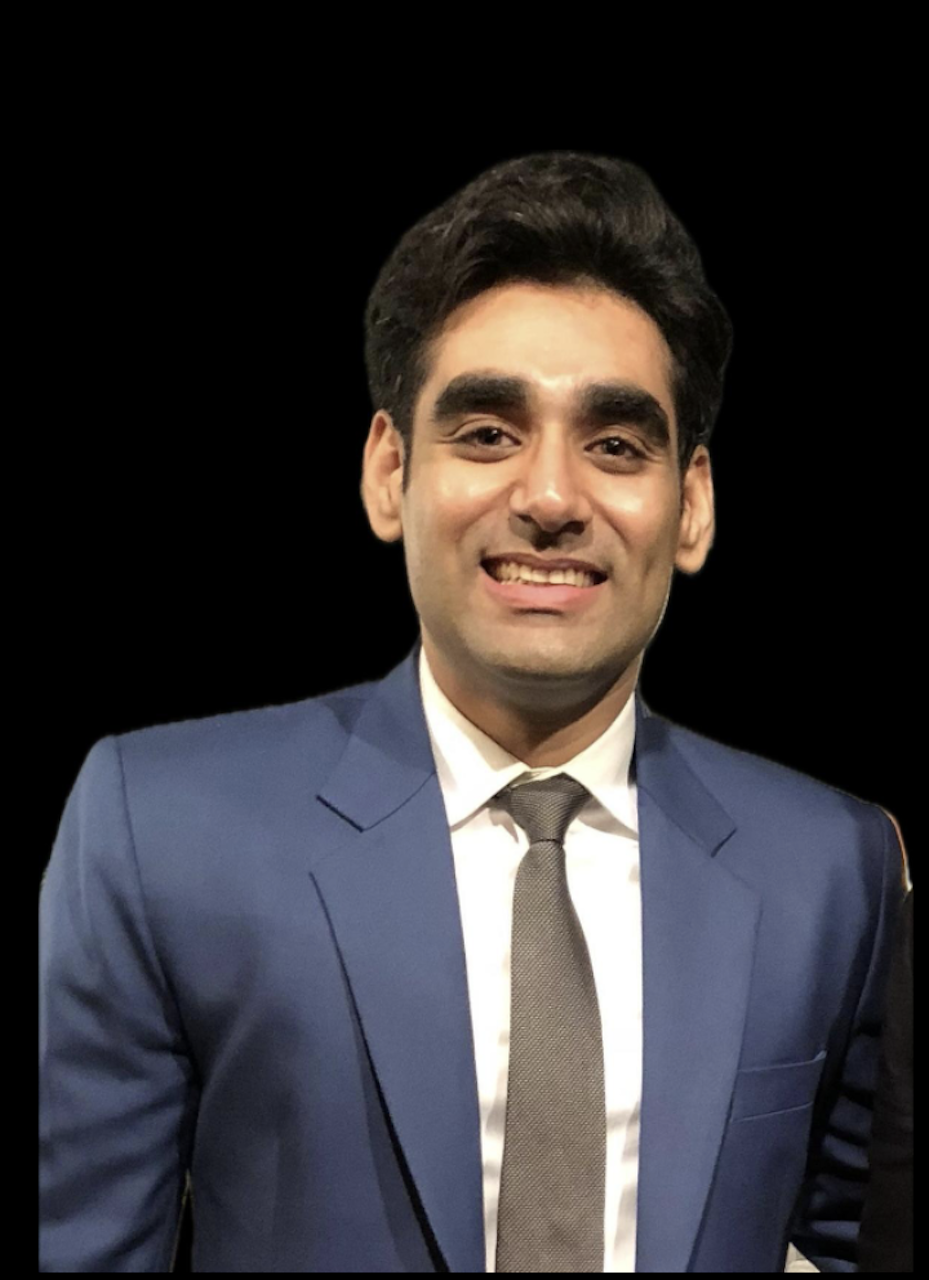 A smiling man in a navy blue suit, white shirt, and gray tie, standing against a black background.